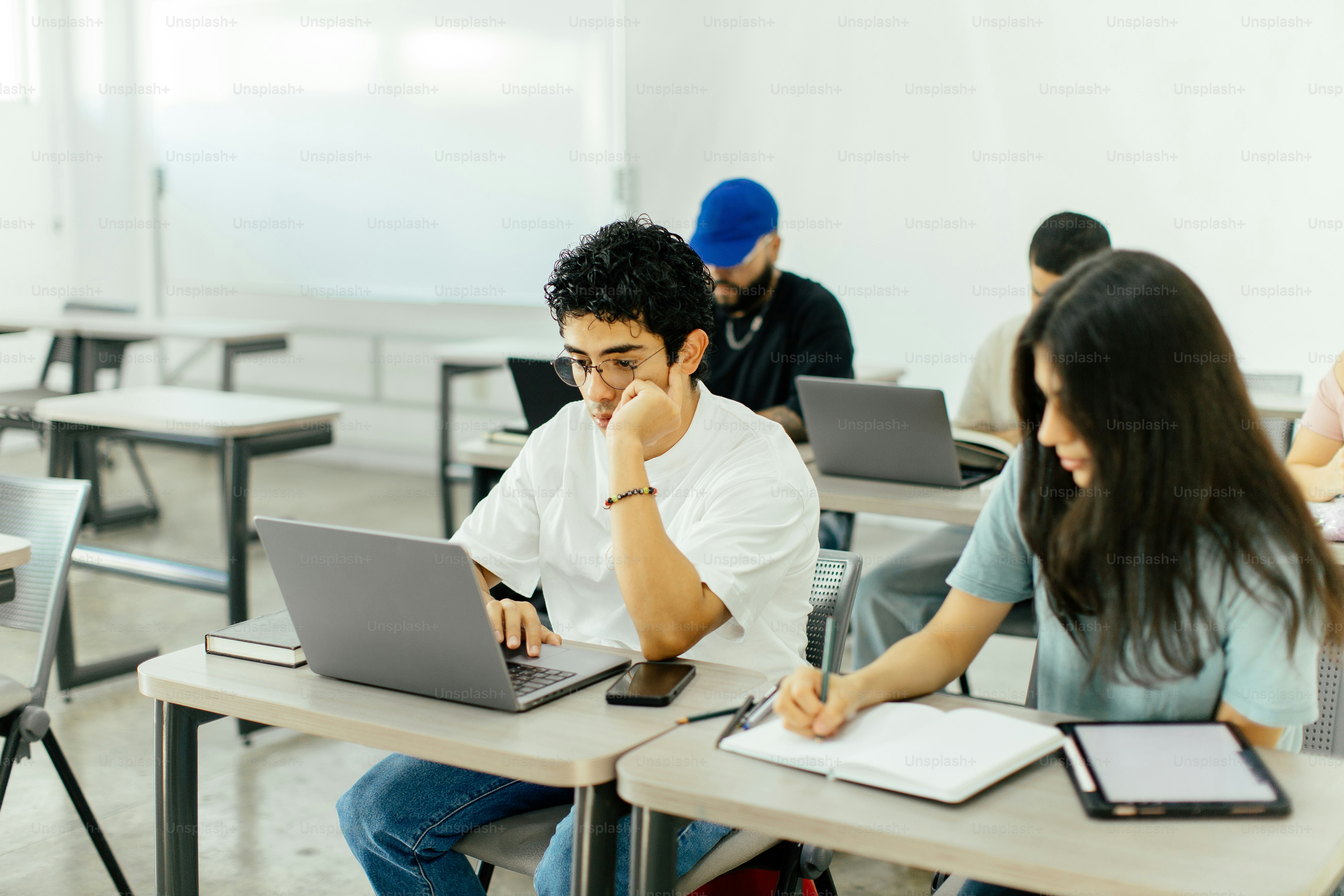 Students work on laptops and write in a classroom.