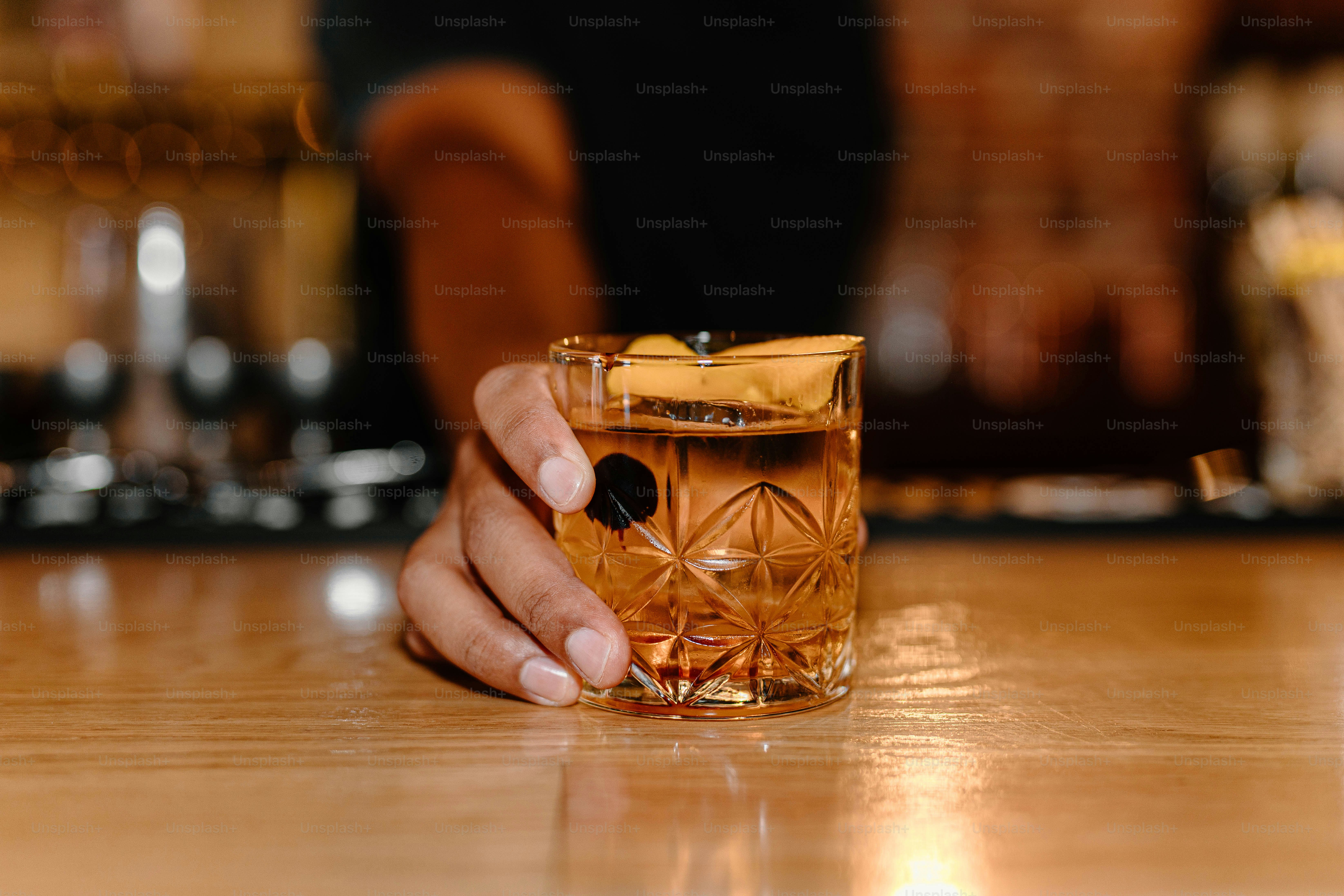 A hand offers a cocktail on a wooden bar.