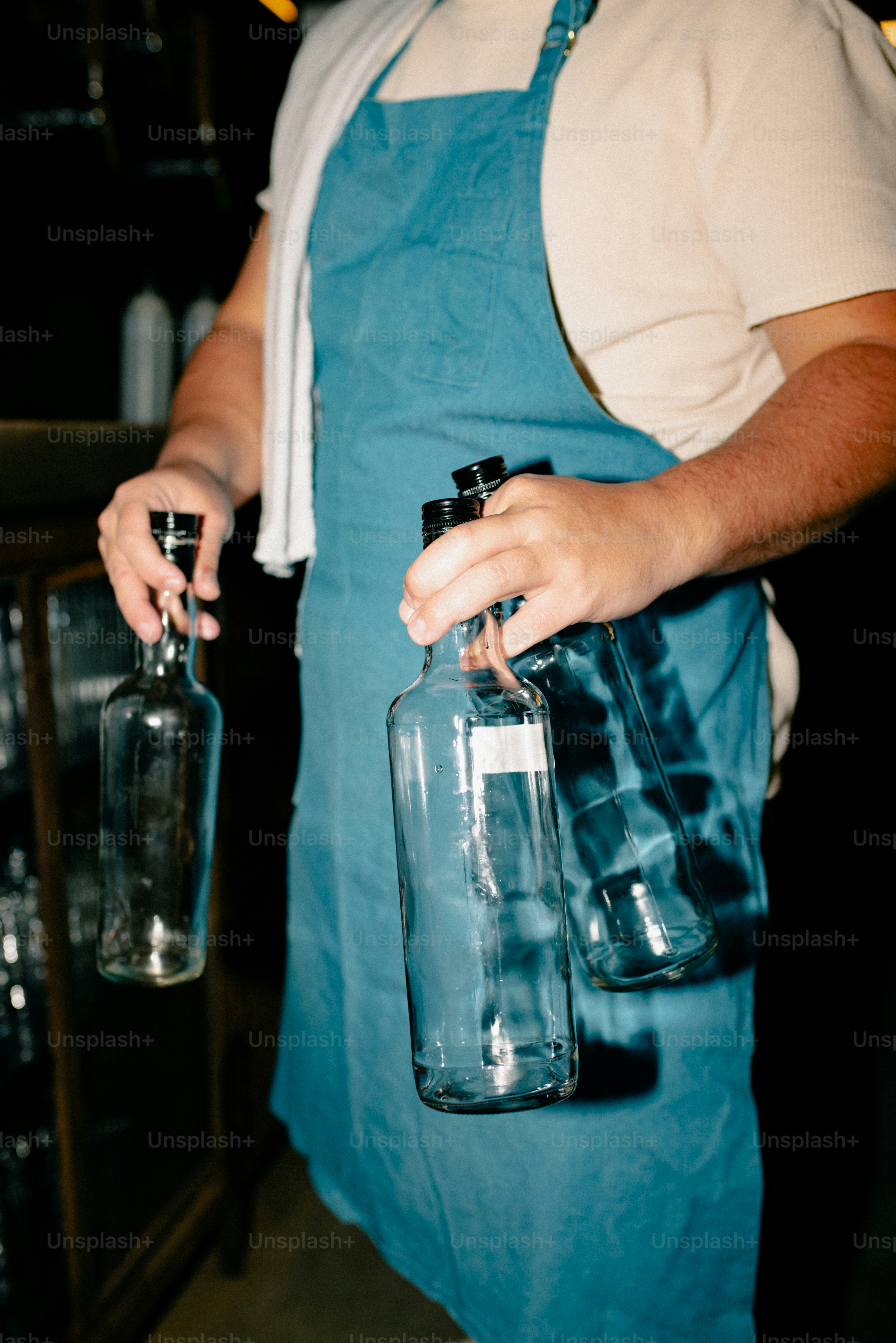 A bartender is holding empty liquor bottles.