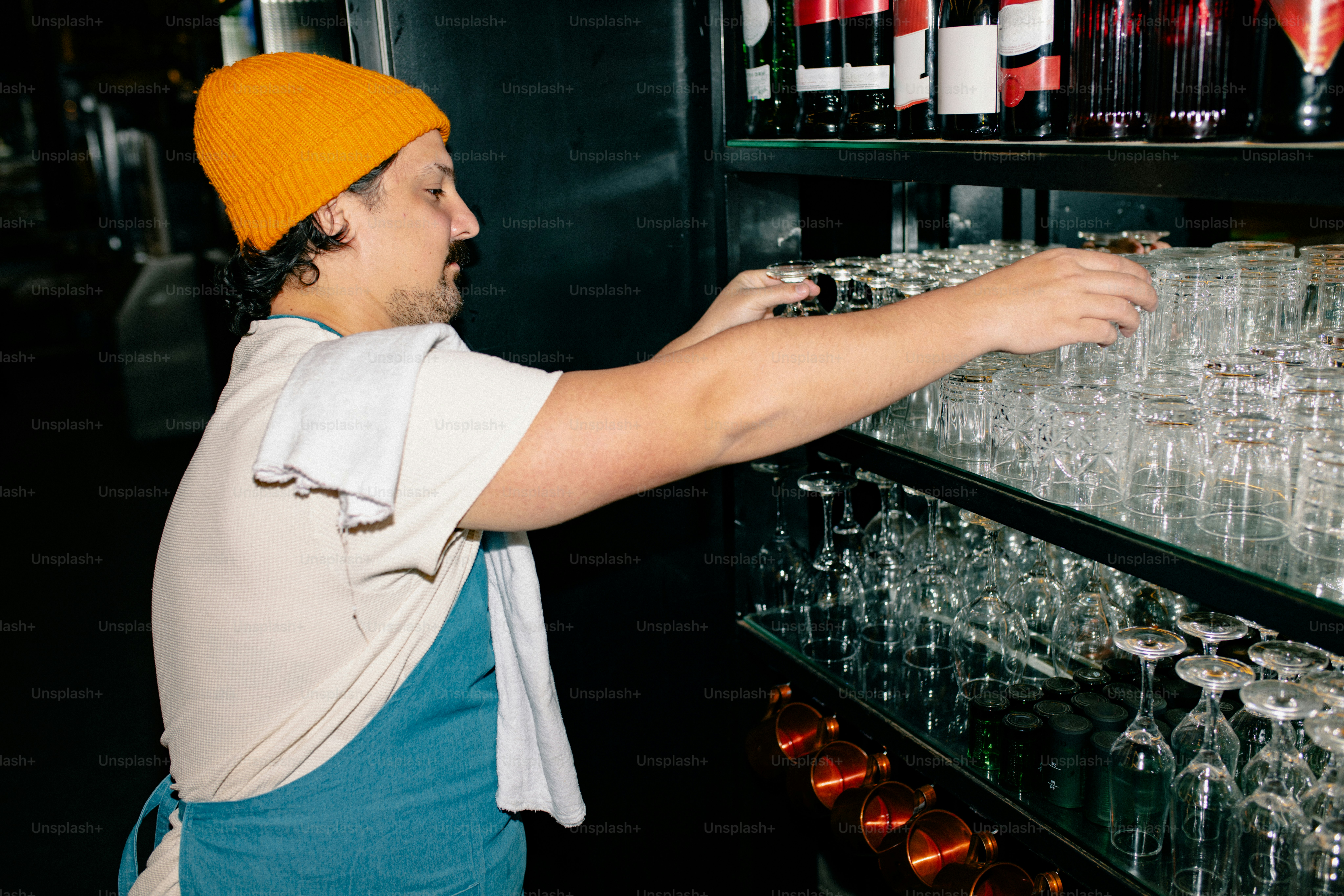 A bartender reaches for glasses behind the bar.