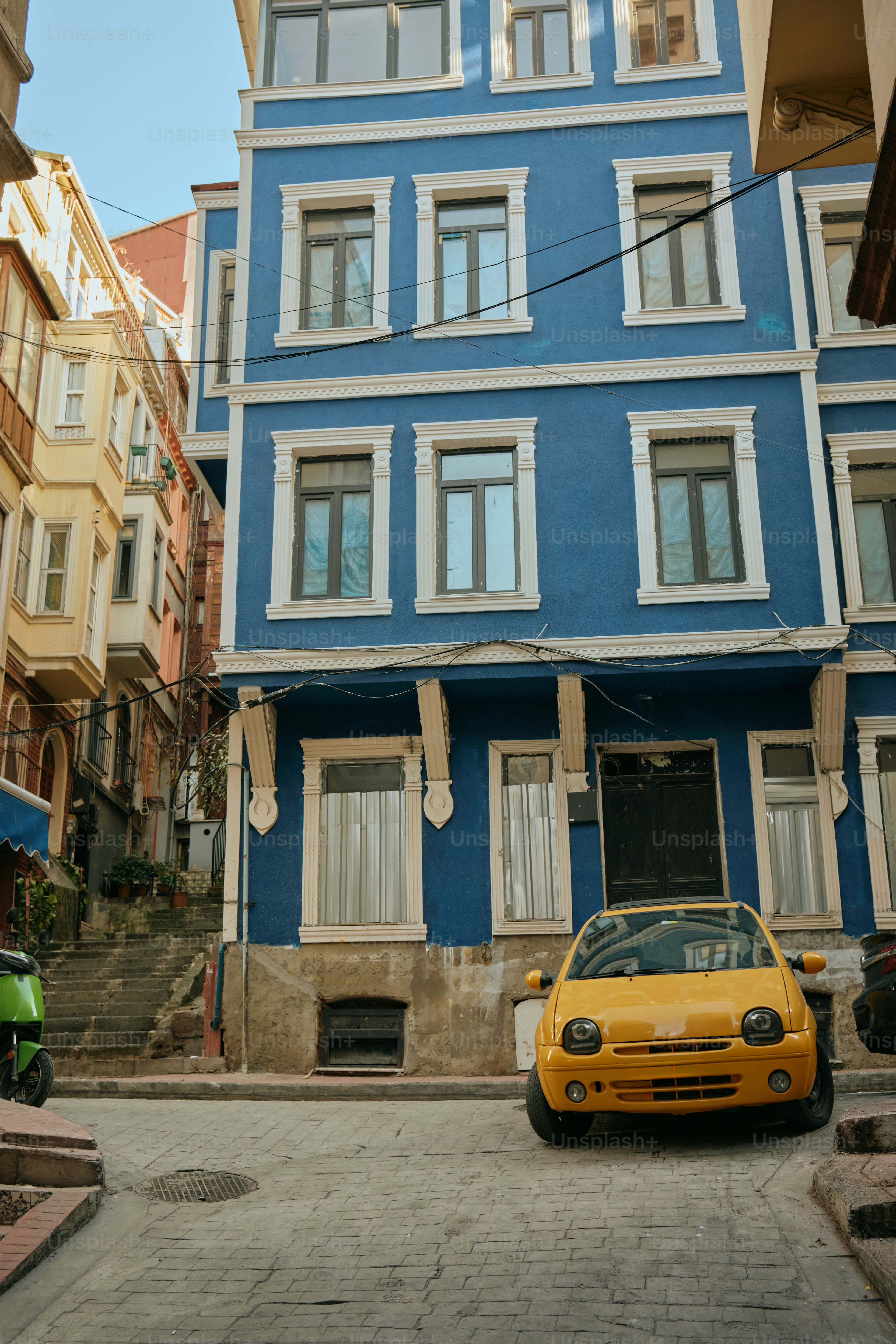 A yellow car sits in front of a blue building.