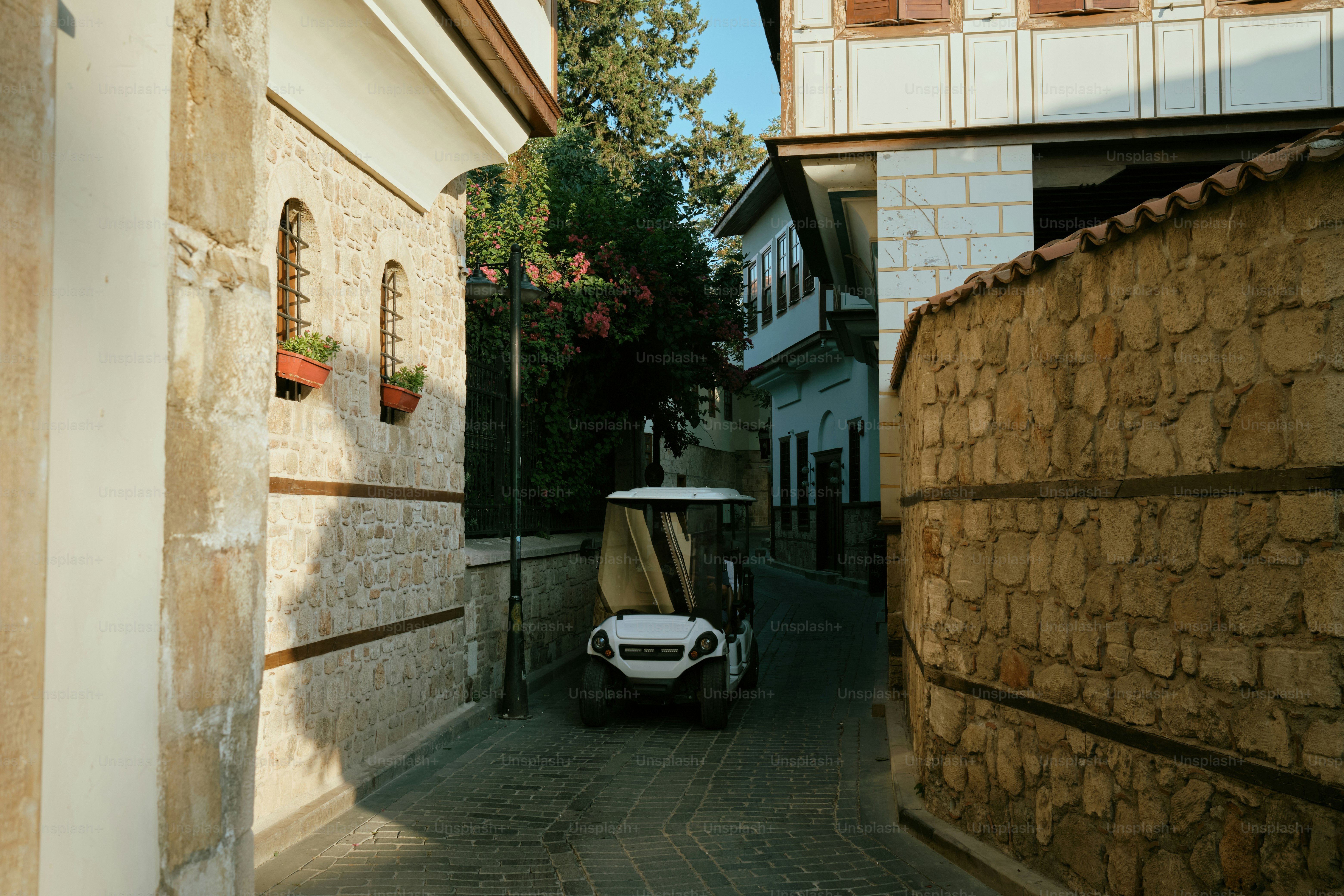 A golf cart drives down a narrow, cobblestone street.