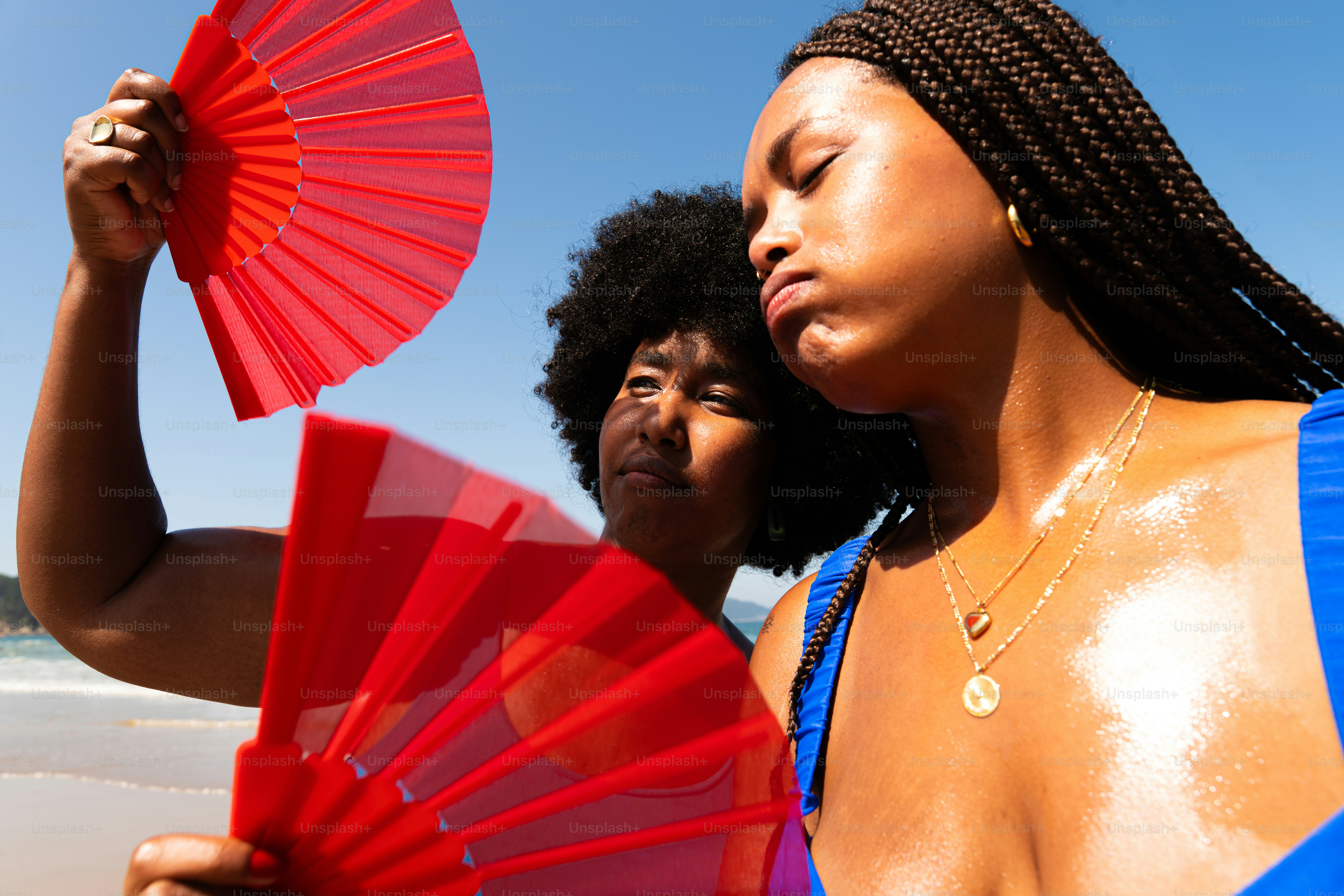 Two women cool off using red fans in the sun.