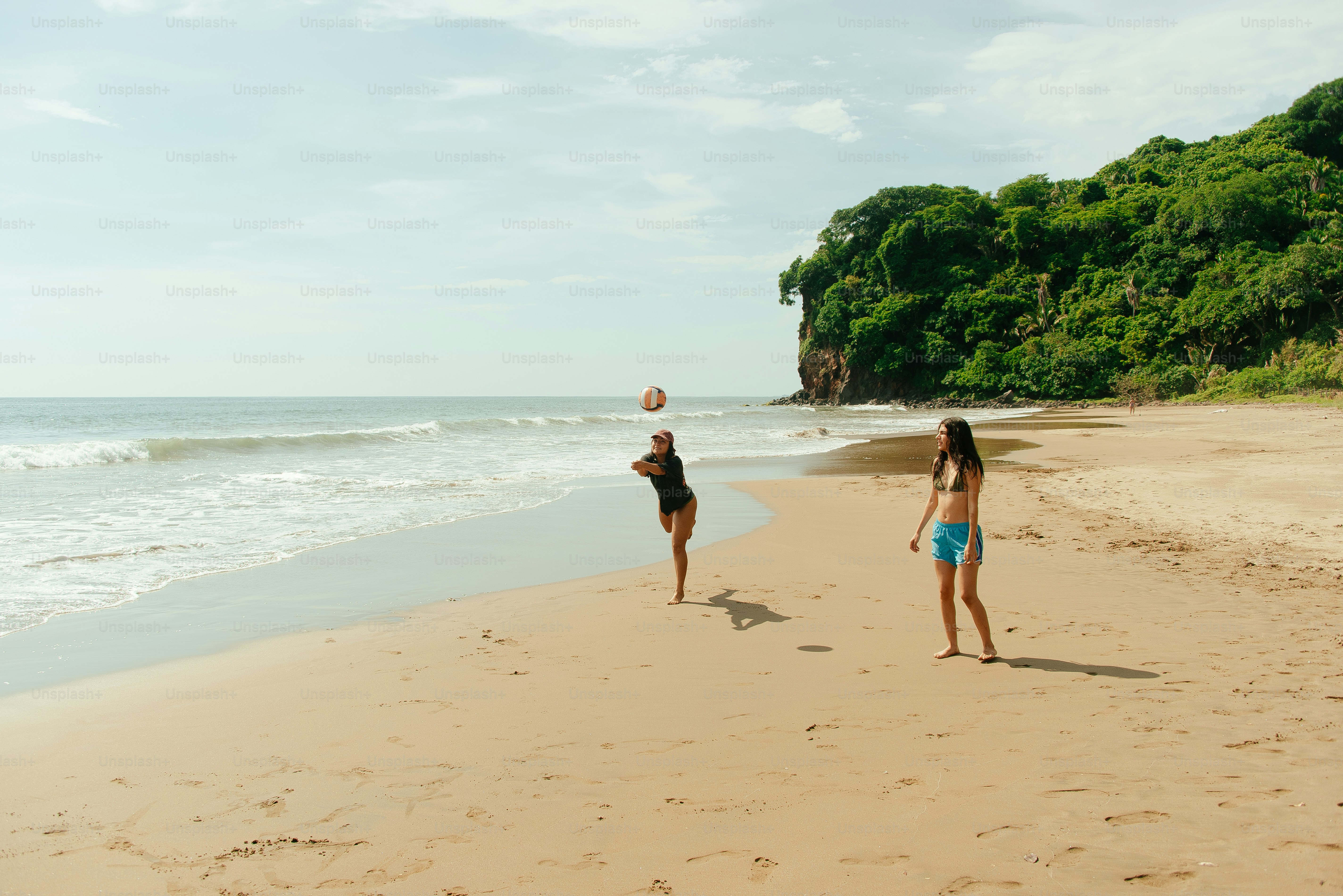 Two women play volleyball on a sunny beach.