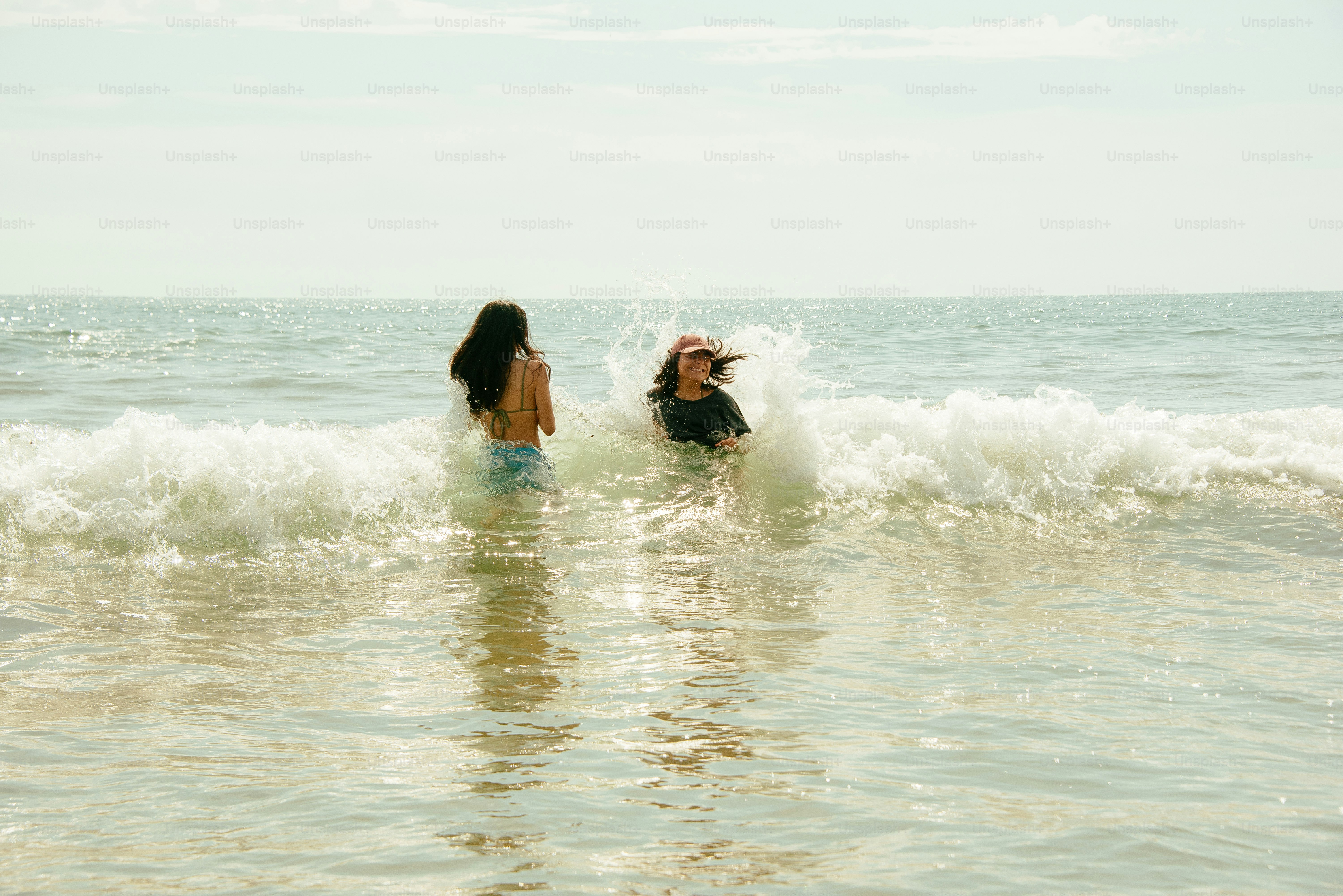 Two people play in the waves at the beach. photo – Beach Image on Unsplash