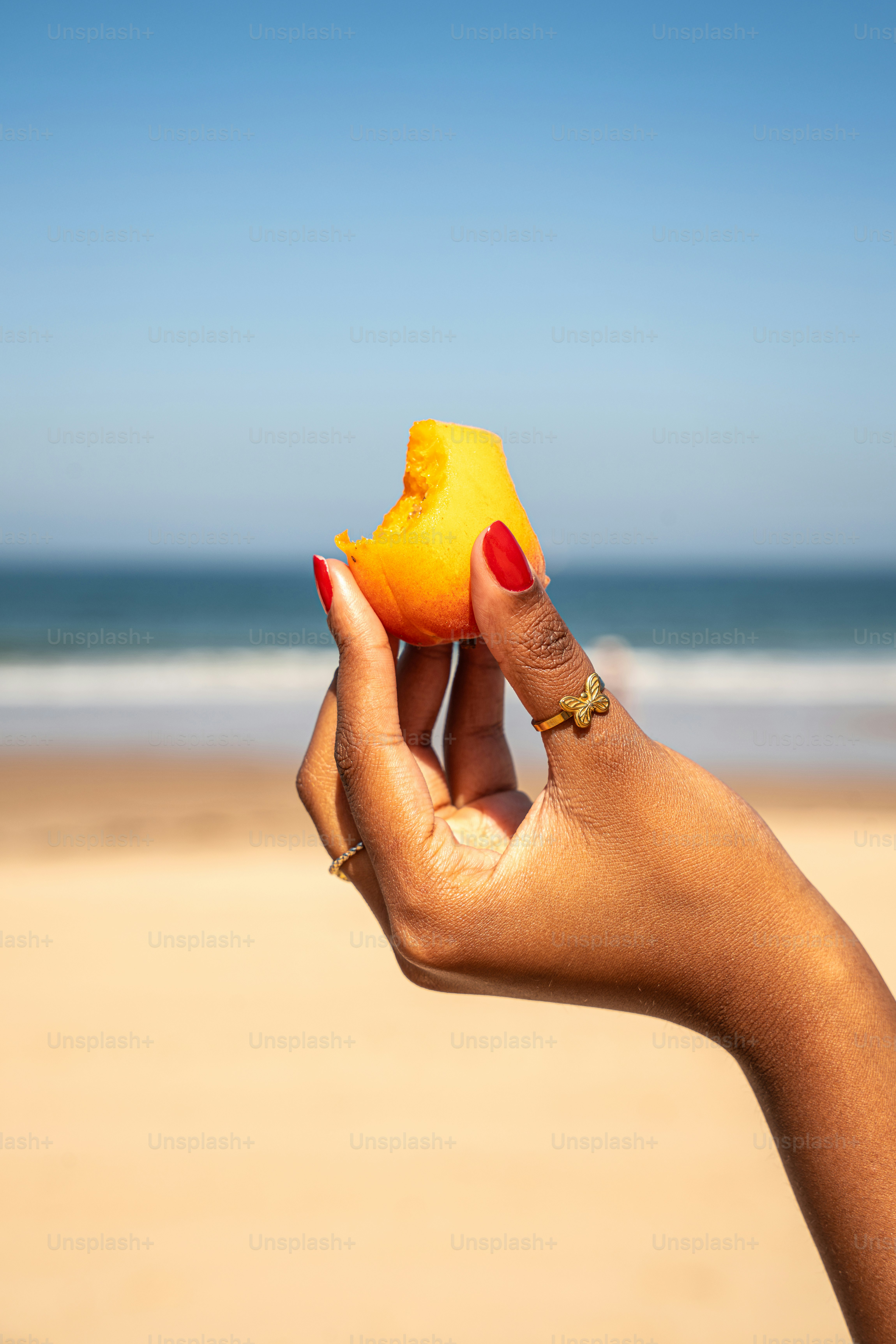 Hand holds a piece of fruit on a beach.