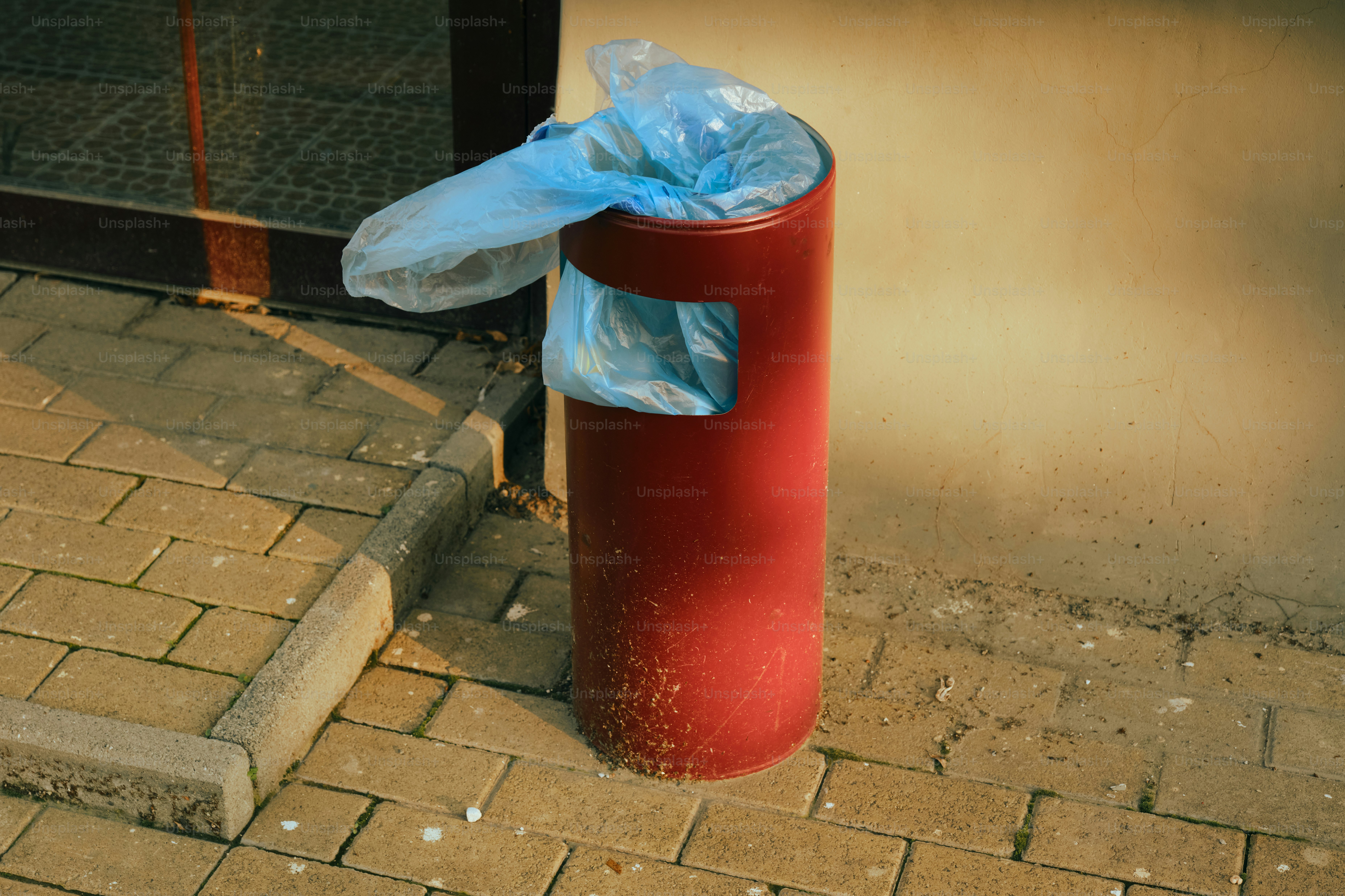A red trash can has a visible blue bag.