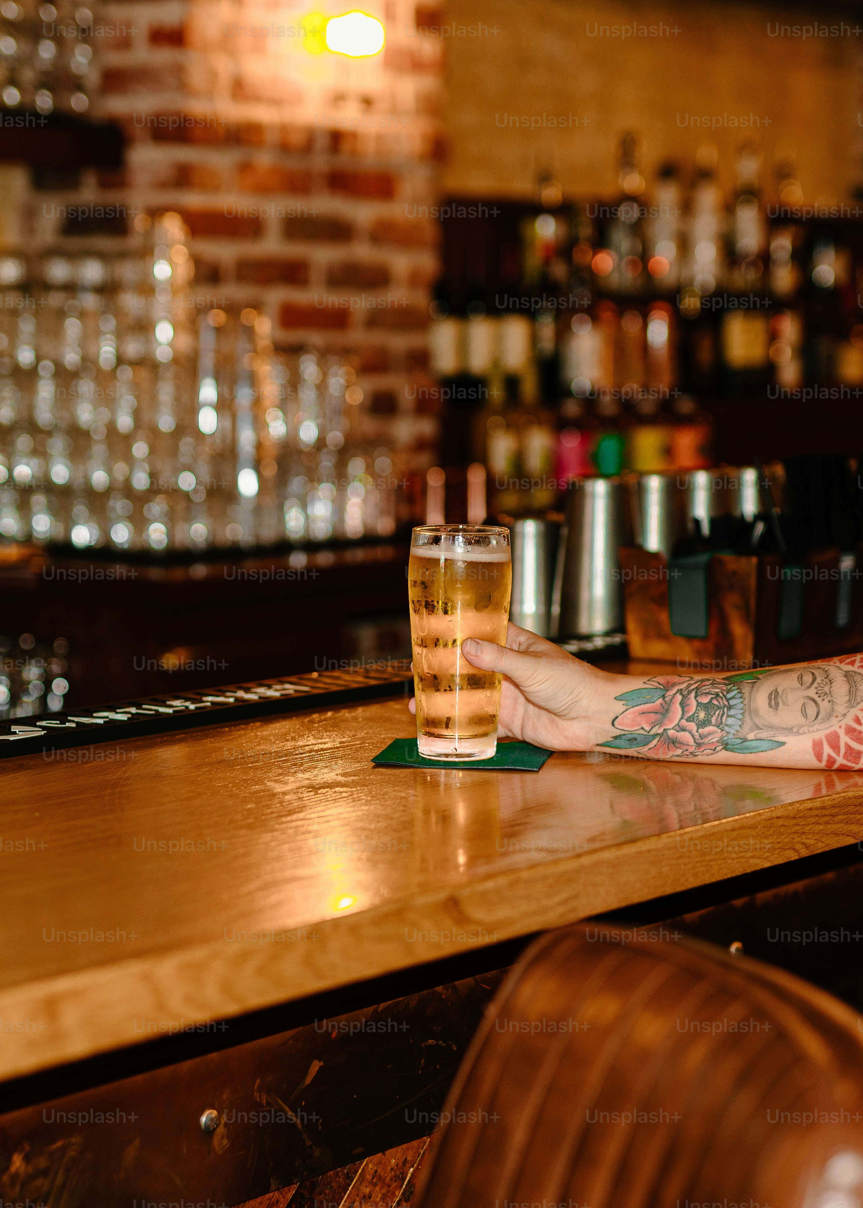A hand holds a glass of beer at the bar.