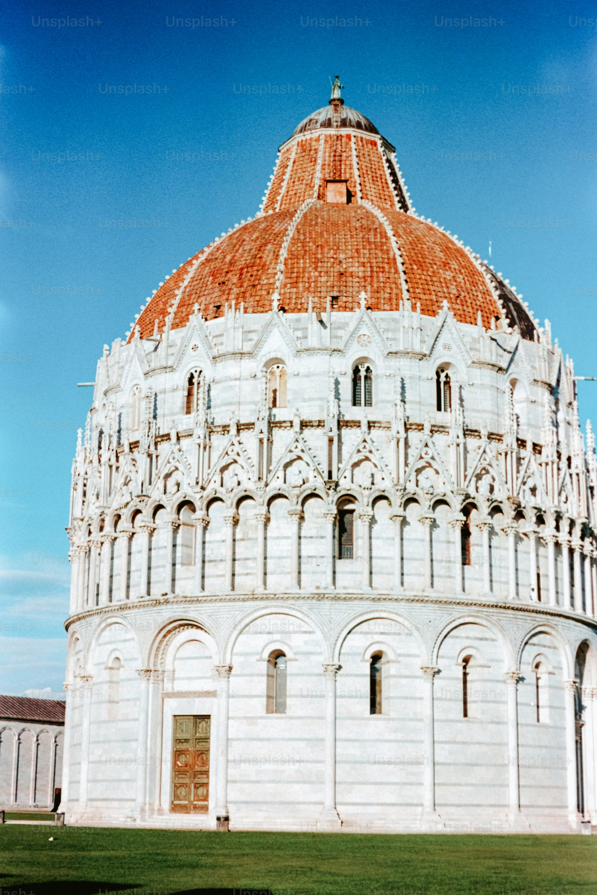 The baptistery of pisa stands beneath a blue sky.