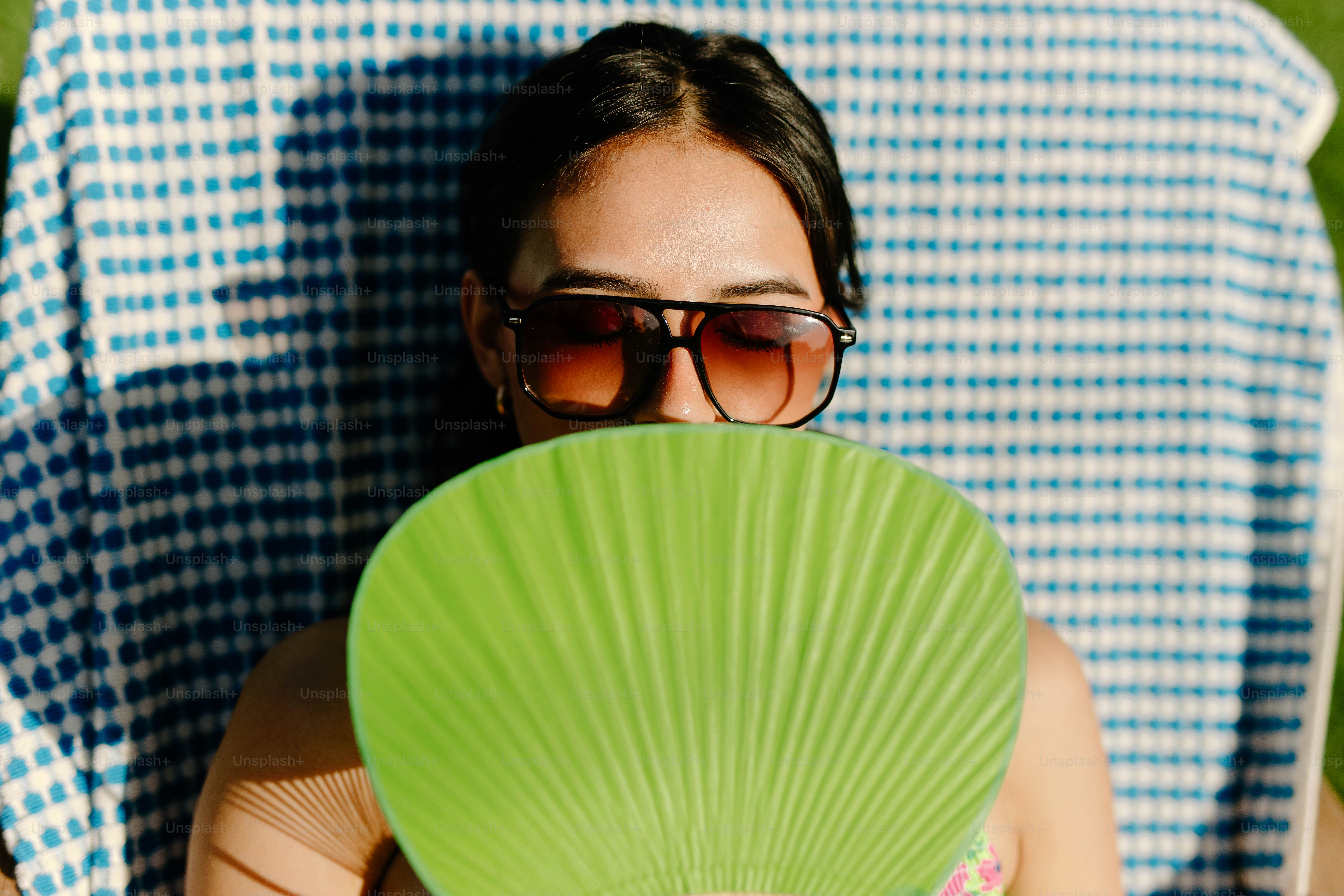 Mulher protege o rosto com um ventilador enquanto toma sol