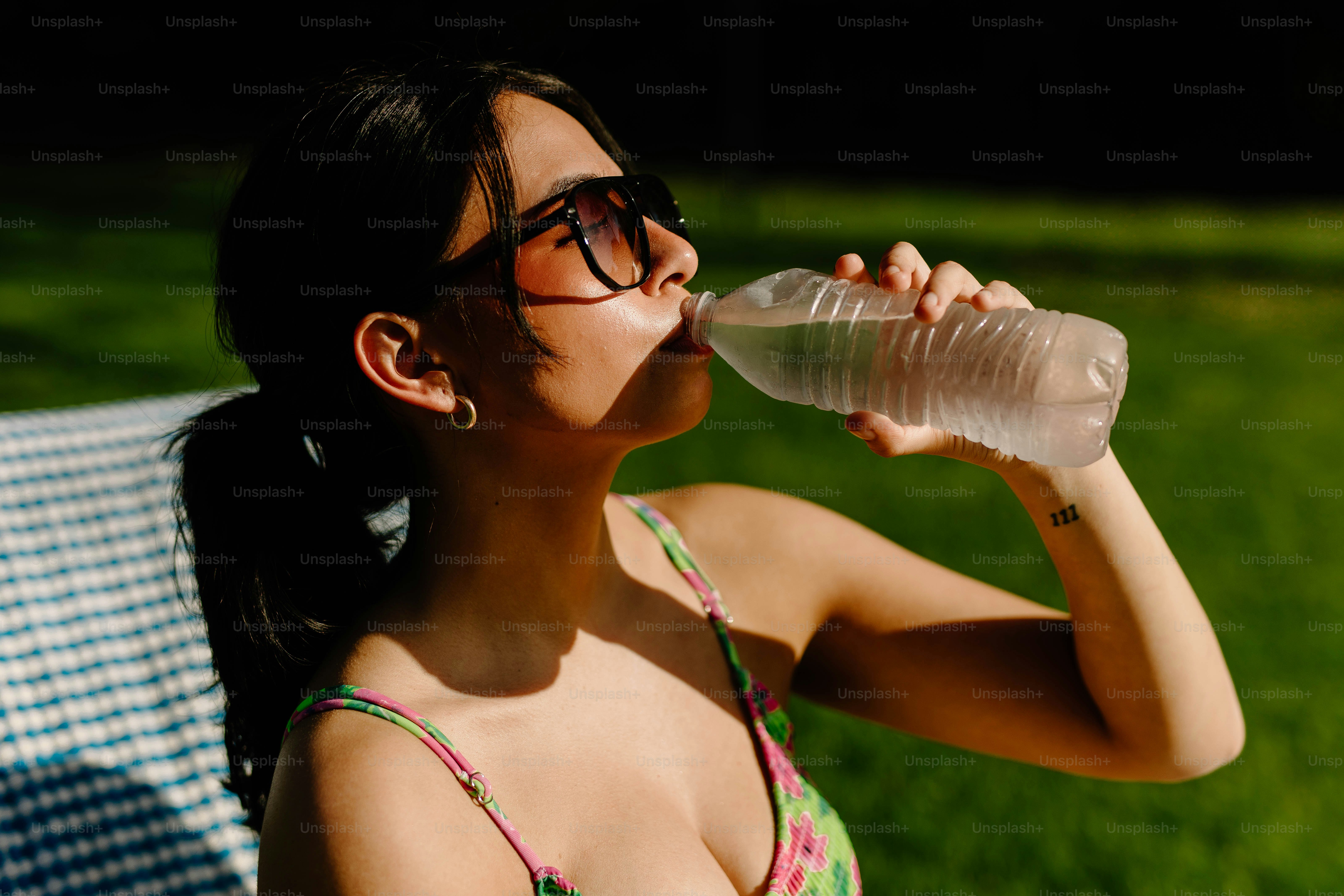 Une femme boit de l’eau à l’extérieur par une journée ensoleillée