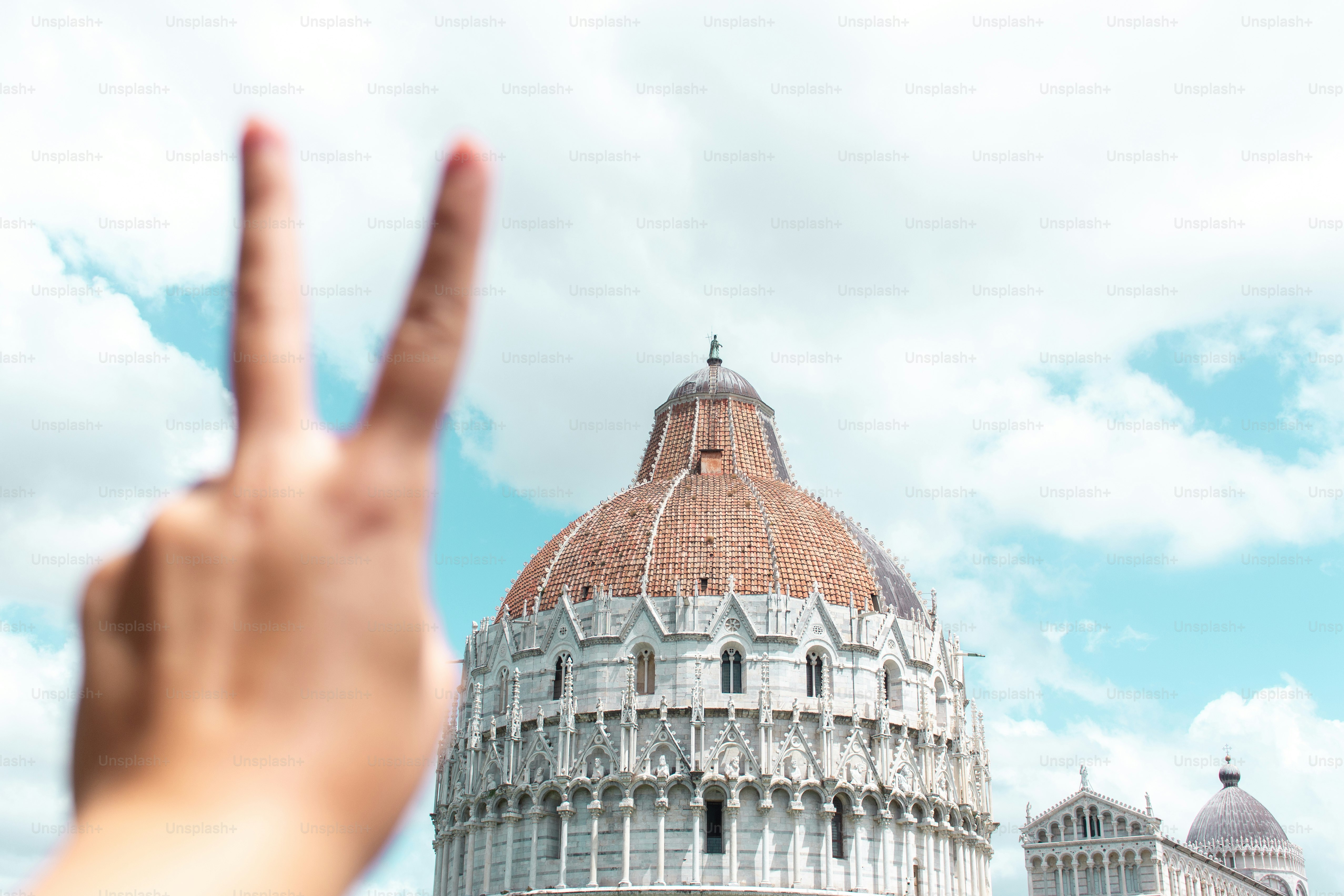 Hand makes peace sign in front of a building.