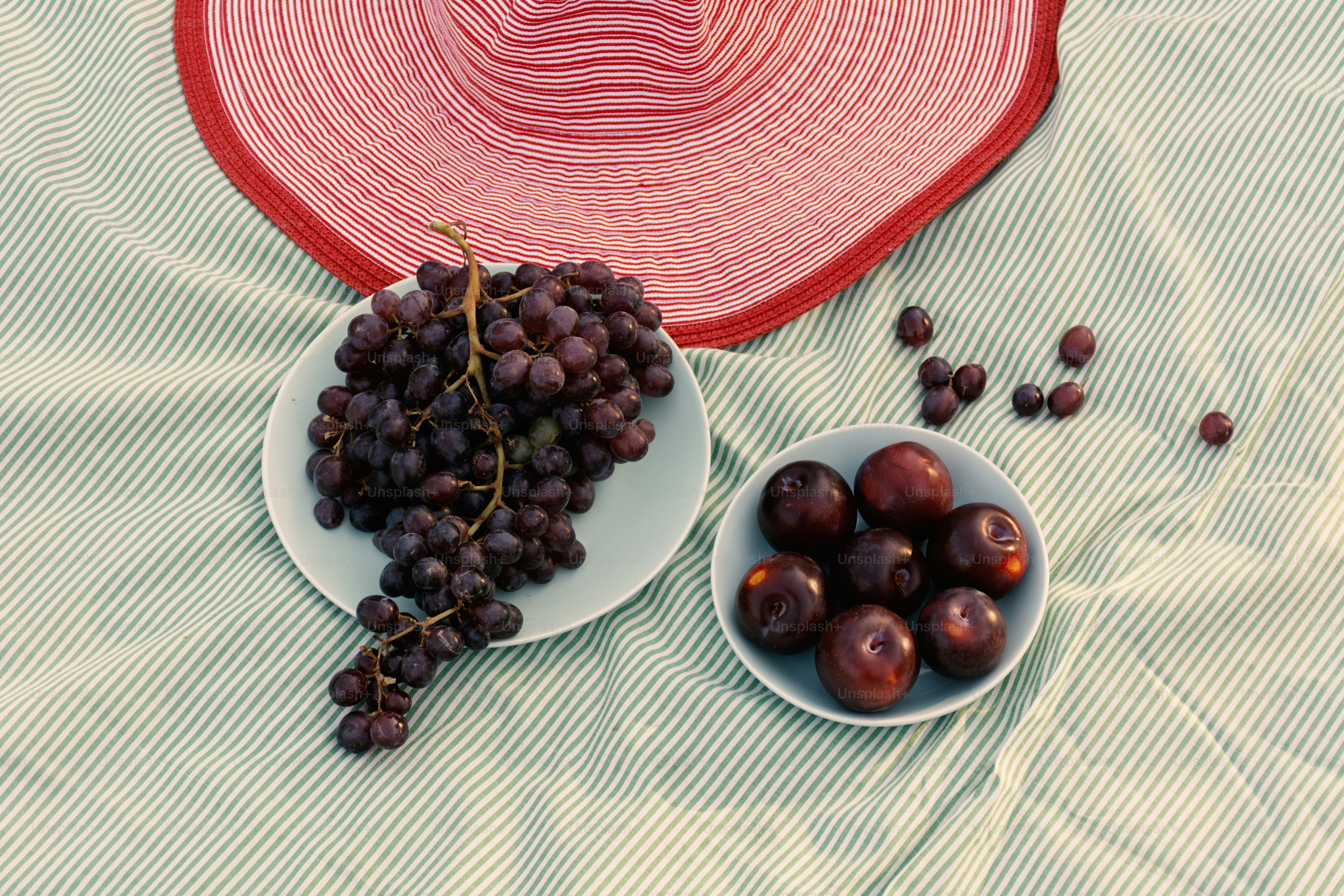 Grapes, plums, and a hat set for a picnic.