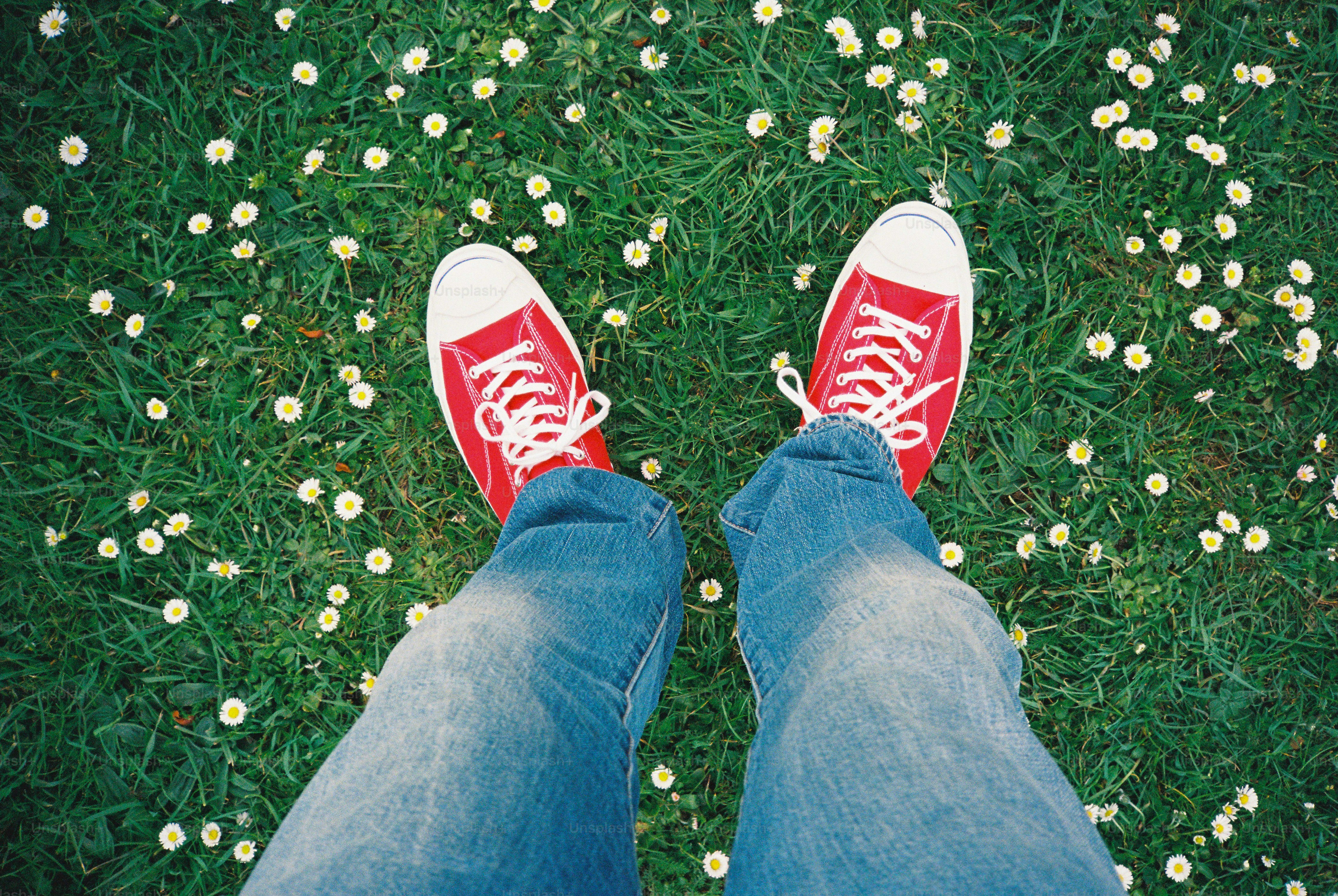 Des chaussures rouges et un jean sur un terrain herbeux.