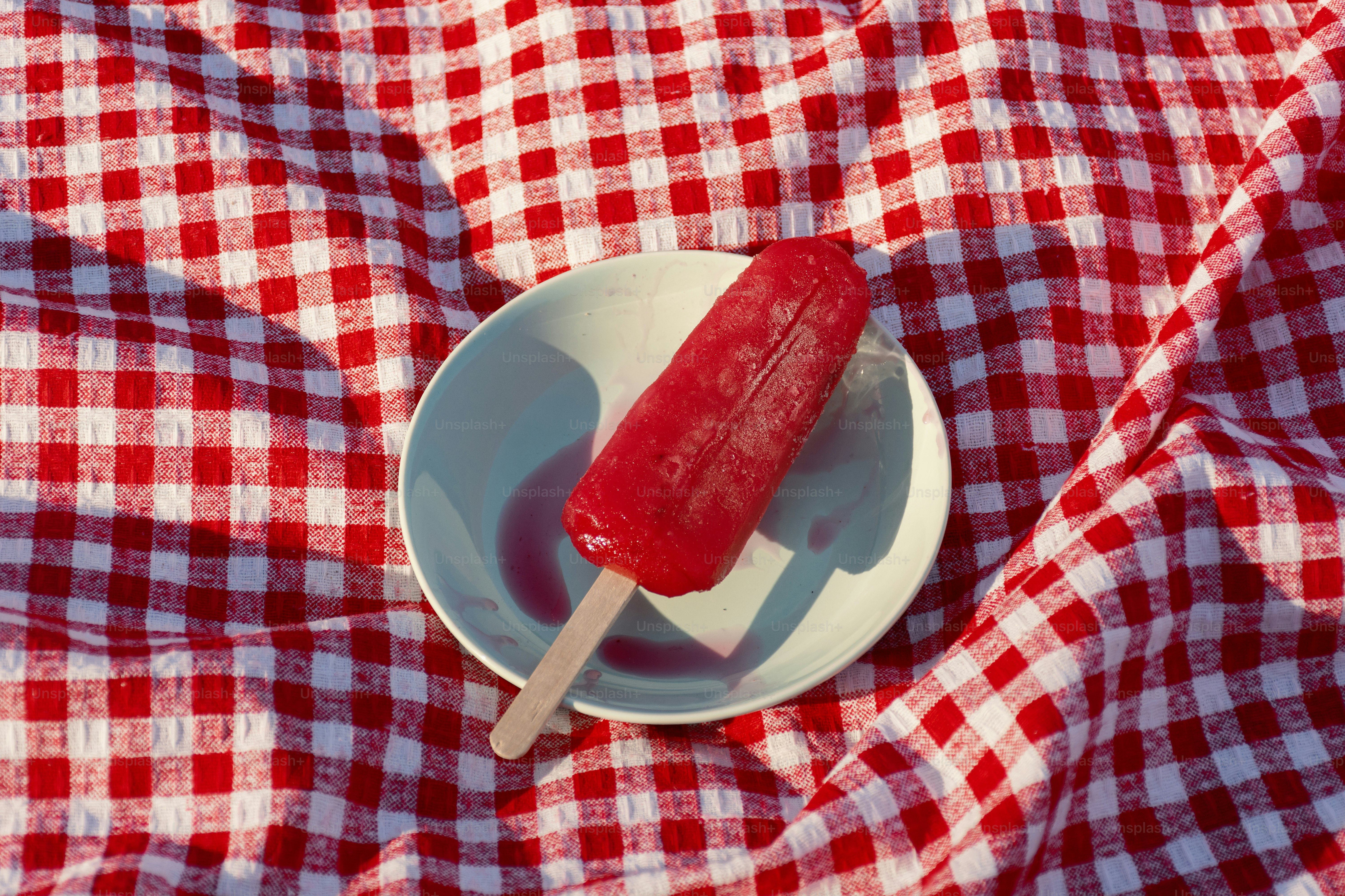 Red popsicle on a plate and plaid.