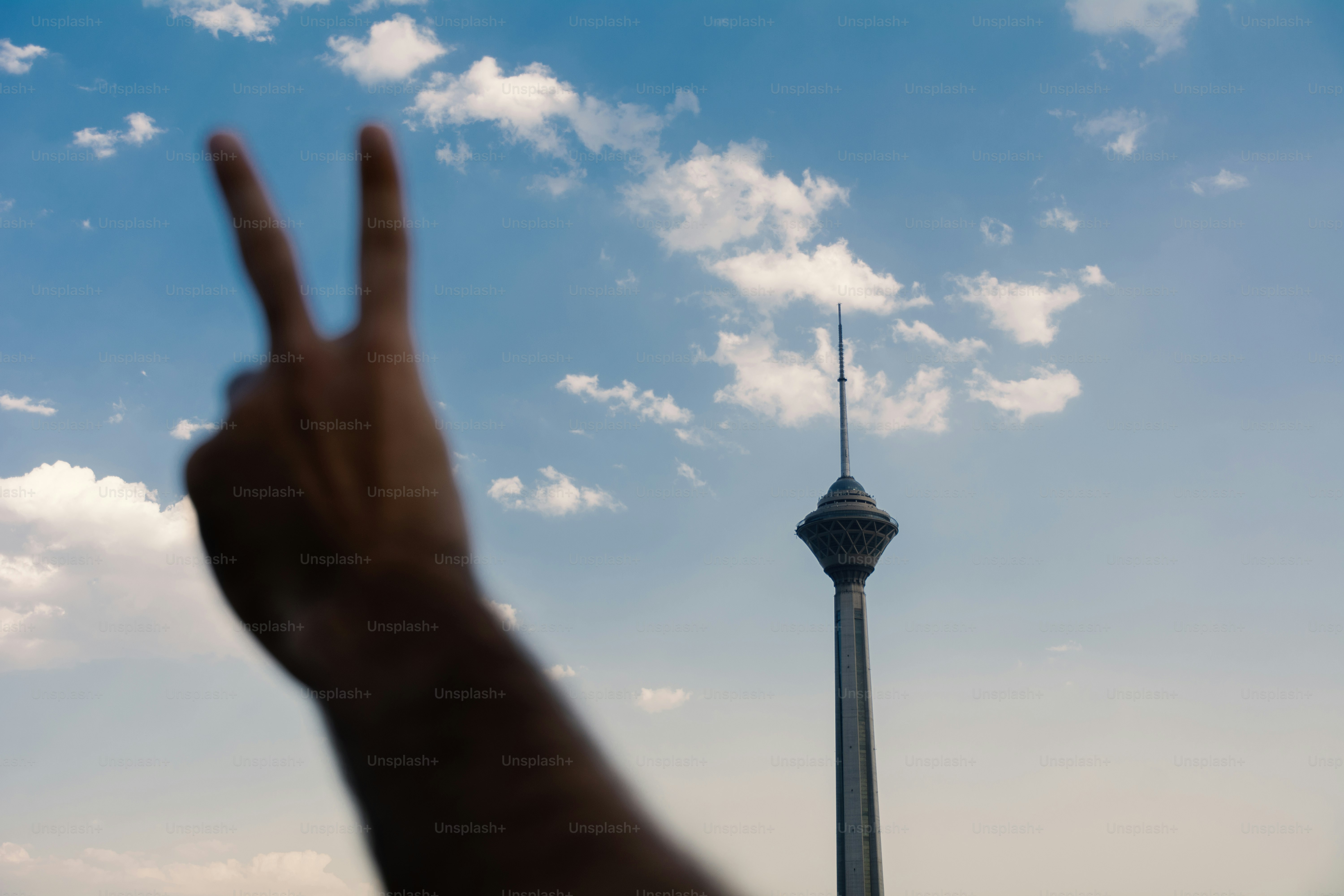 Haciendo a mano el signo de la paz con la torre azadi detrás.