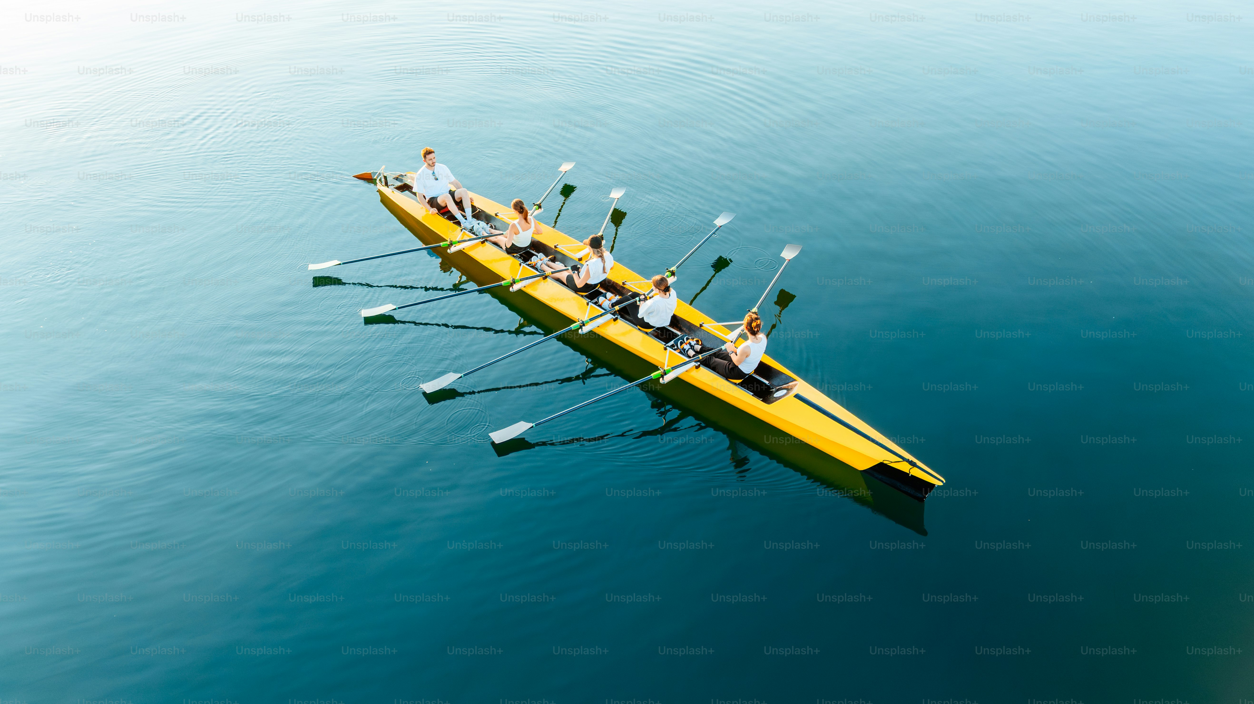 Rowers navigate a yellow boat on tranquil waters