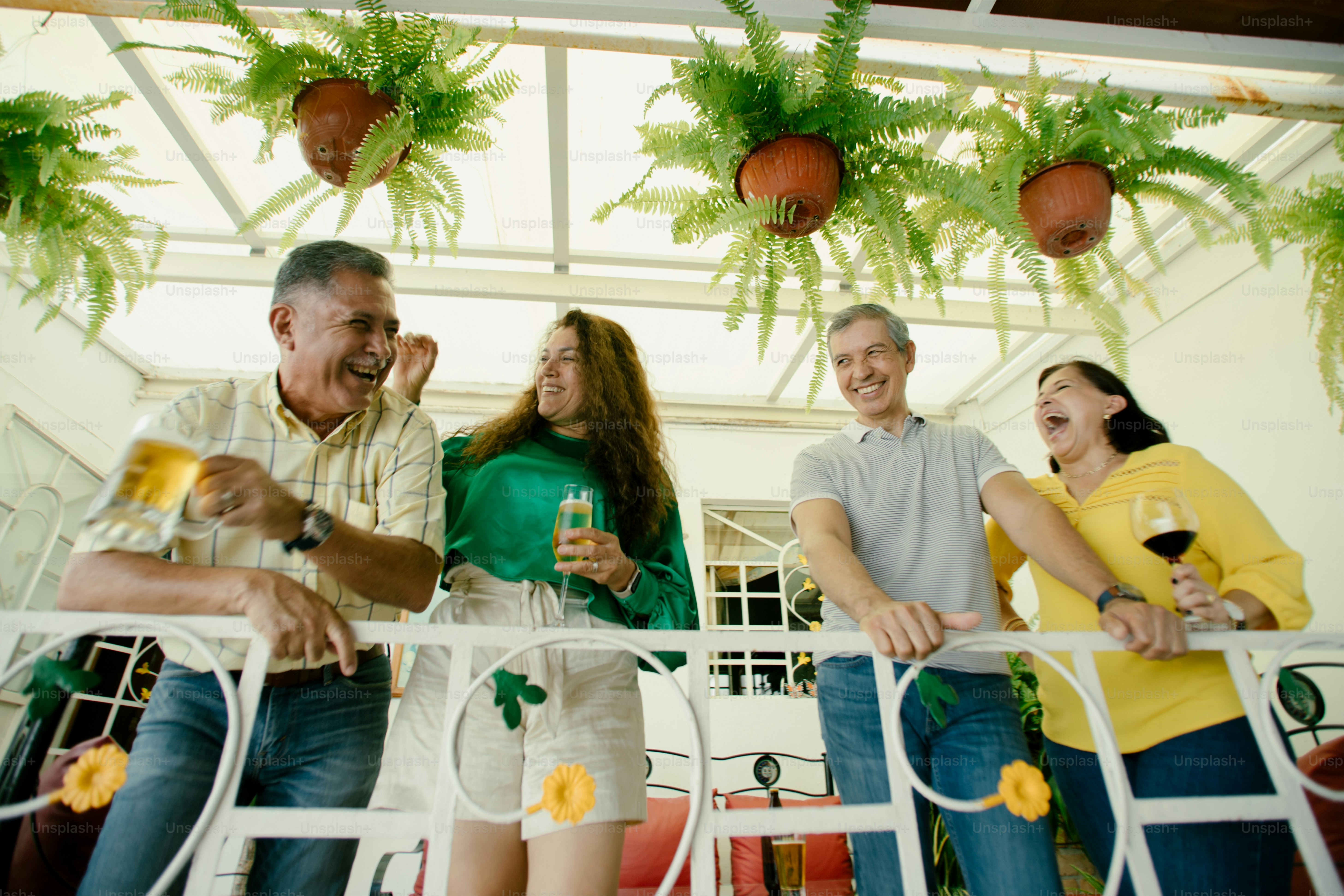 Friends laugh and enjoy drinks on a balcony.