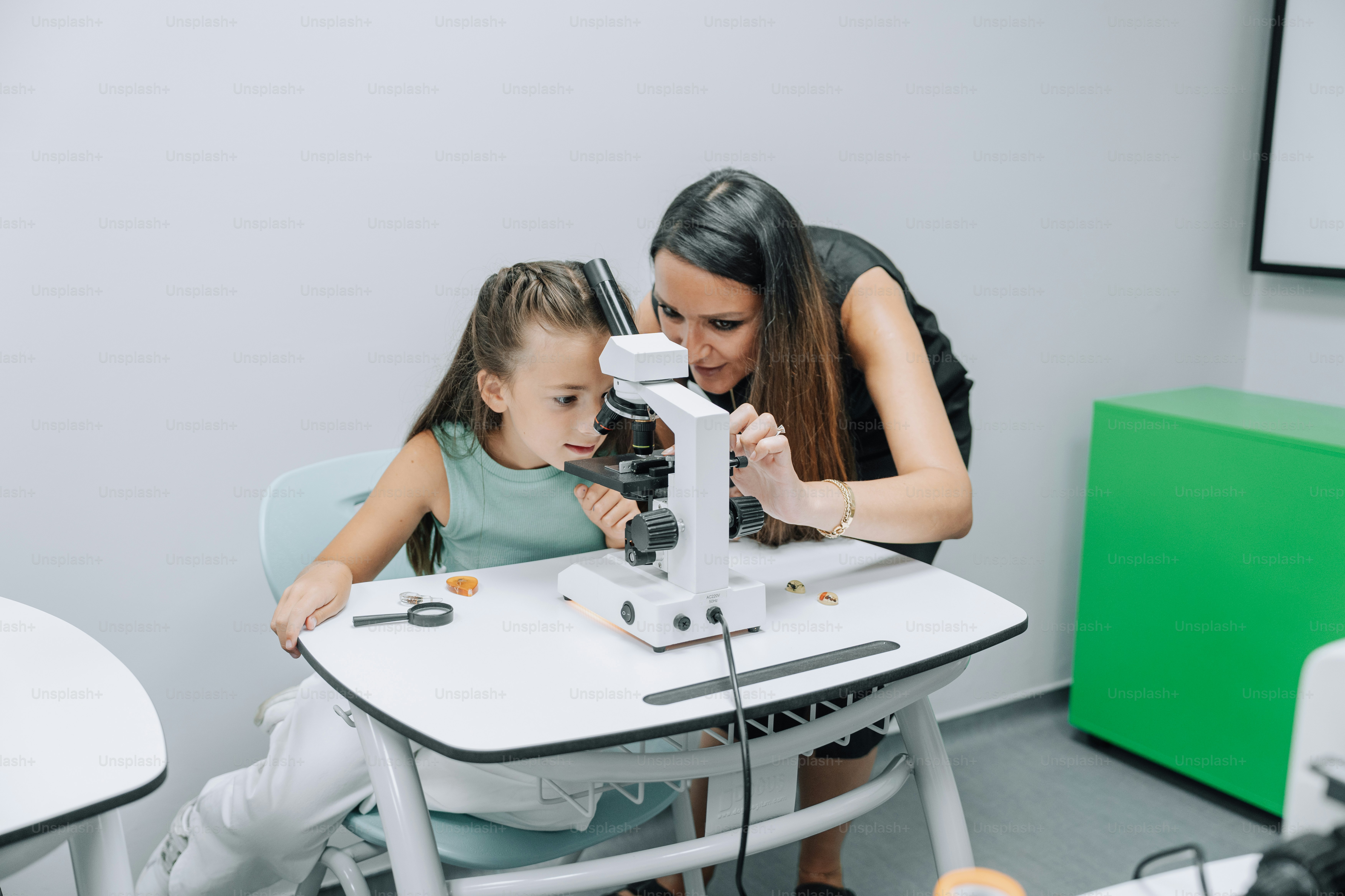 A teacher shows a girl how to use a microscope.