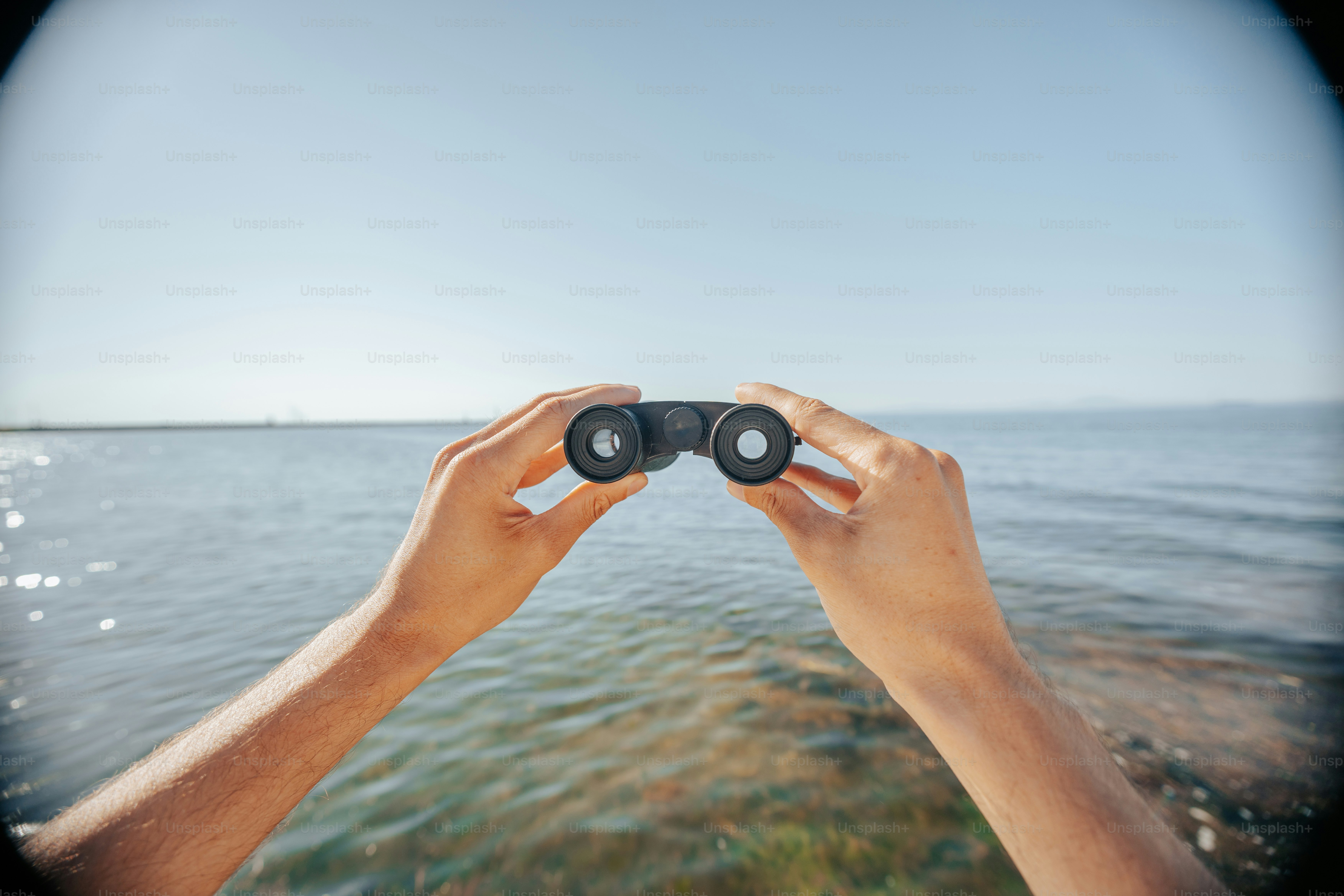 Hands hold binoculars, looking out over the water.