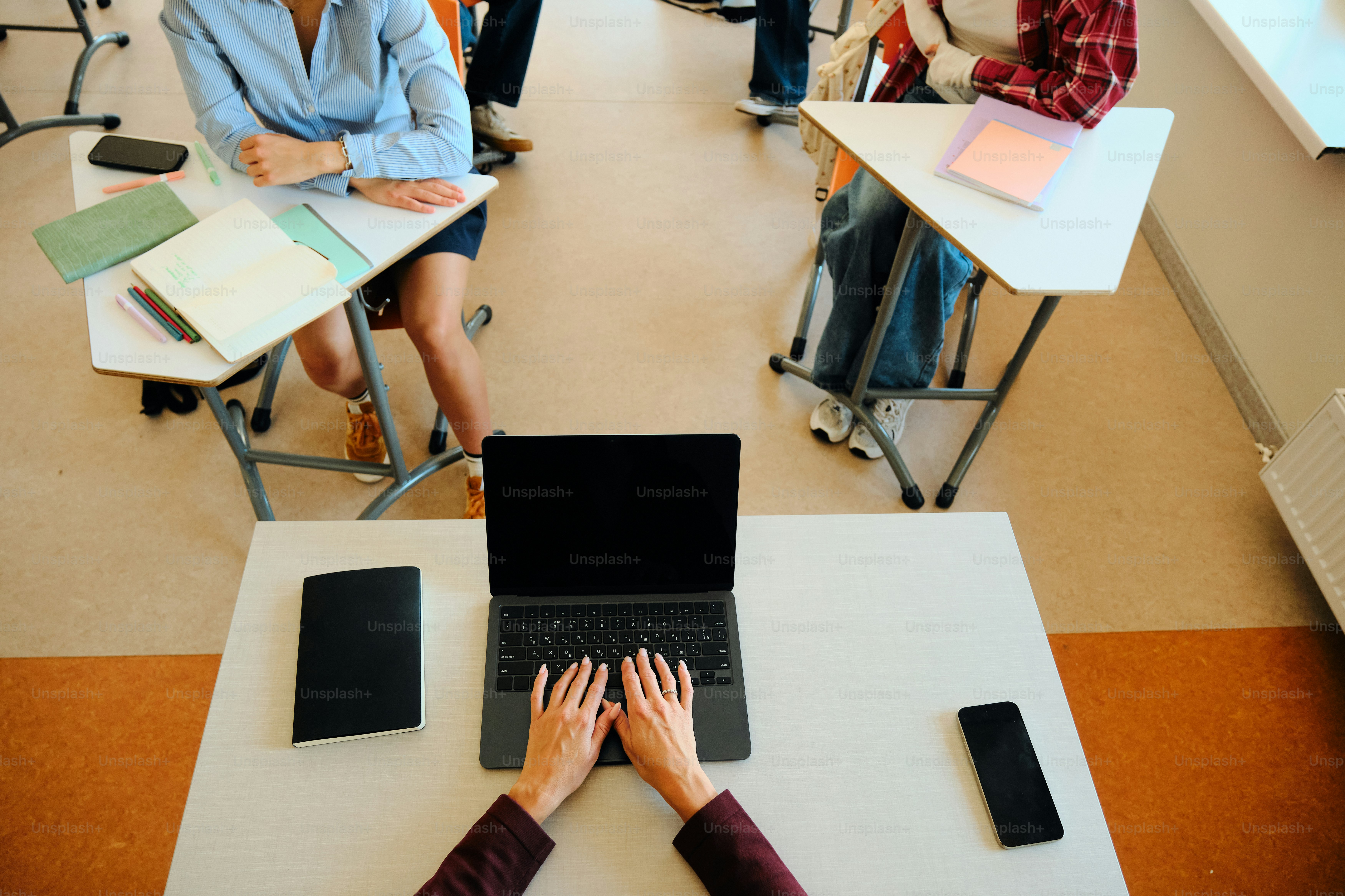 A person is typing on a laptop in a classroom.