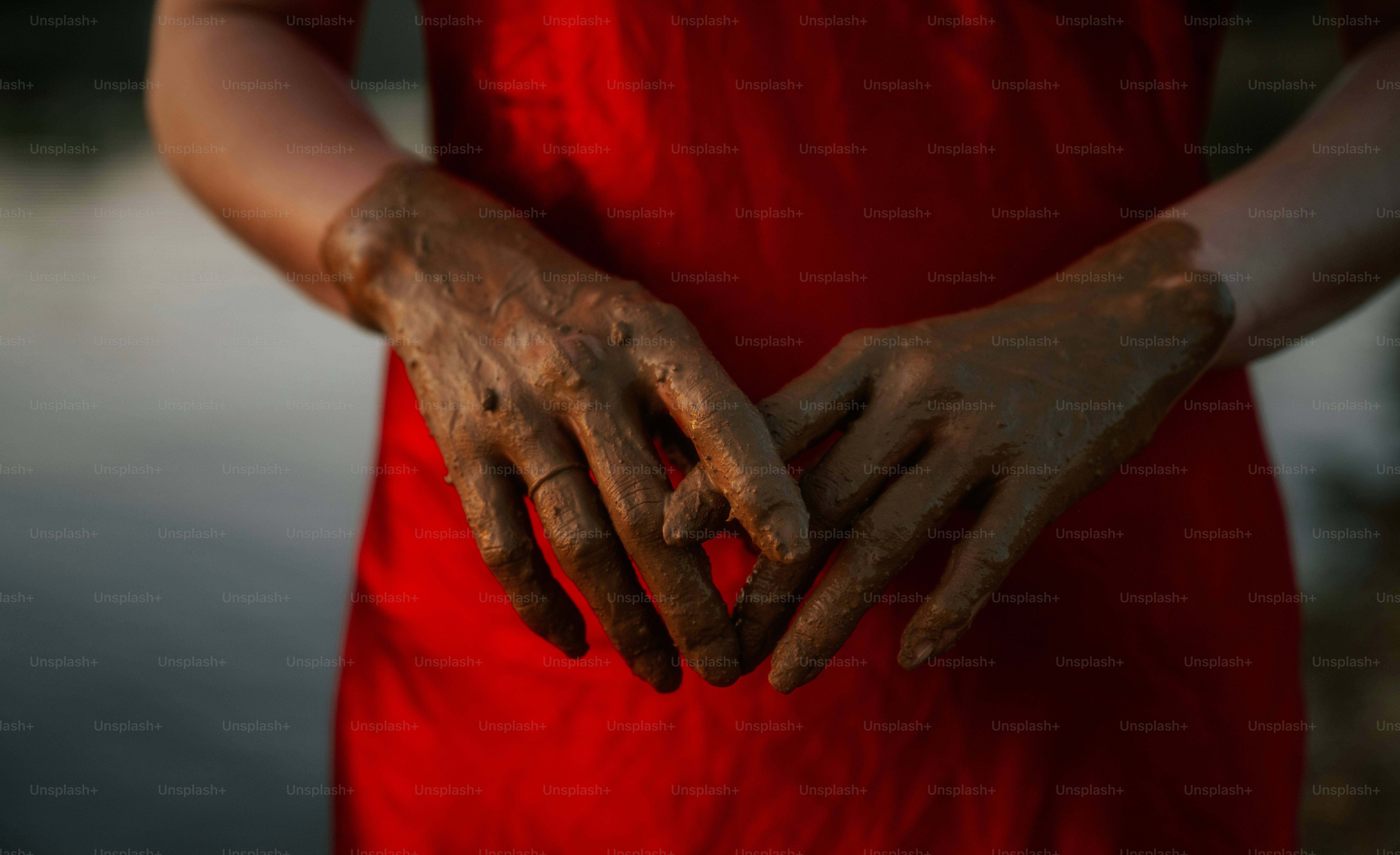 Muddy hands clasped in front of a red dress.