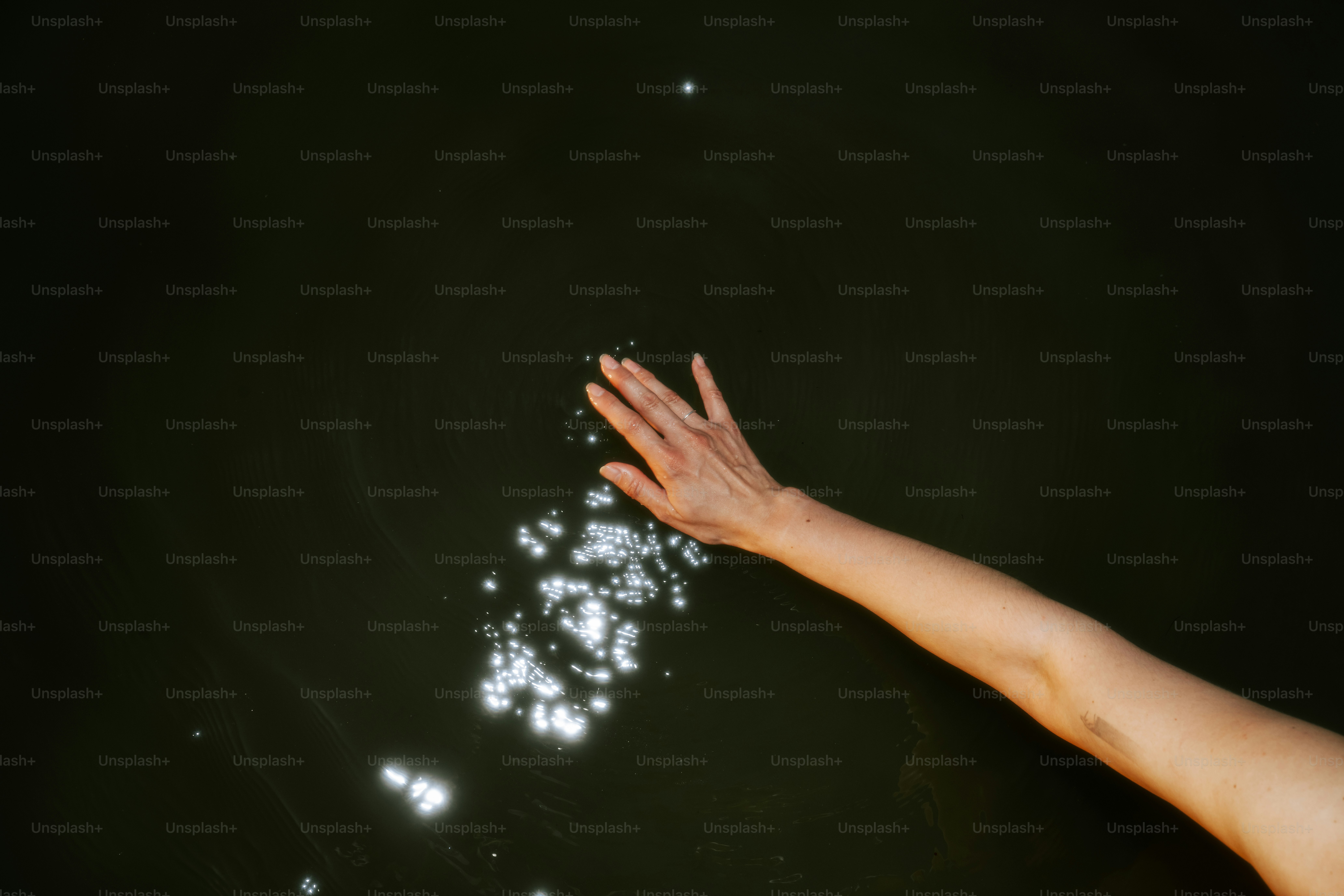 Eine Hand berührt Wasser mit glitzerndem Sonnenlicht.