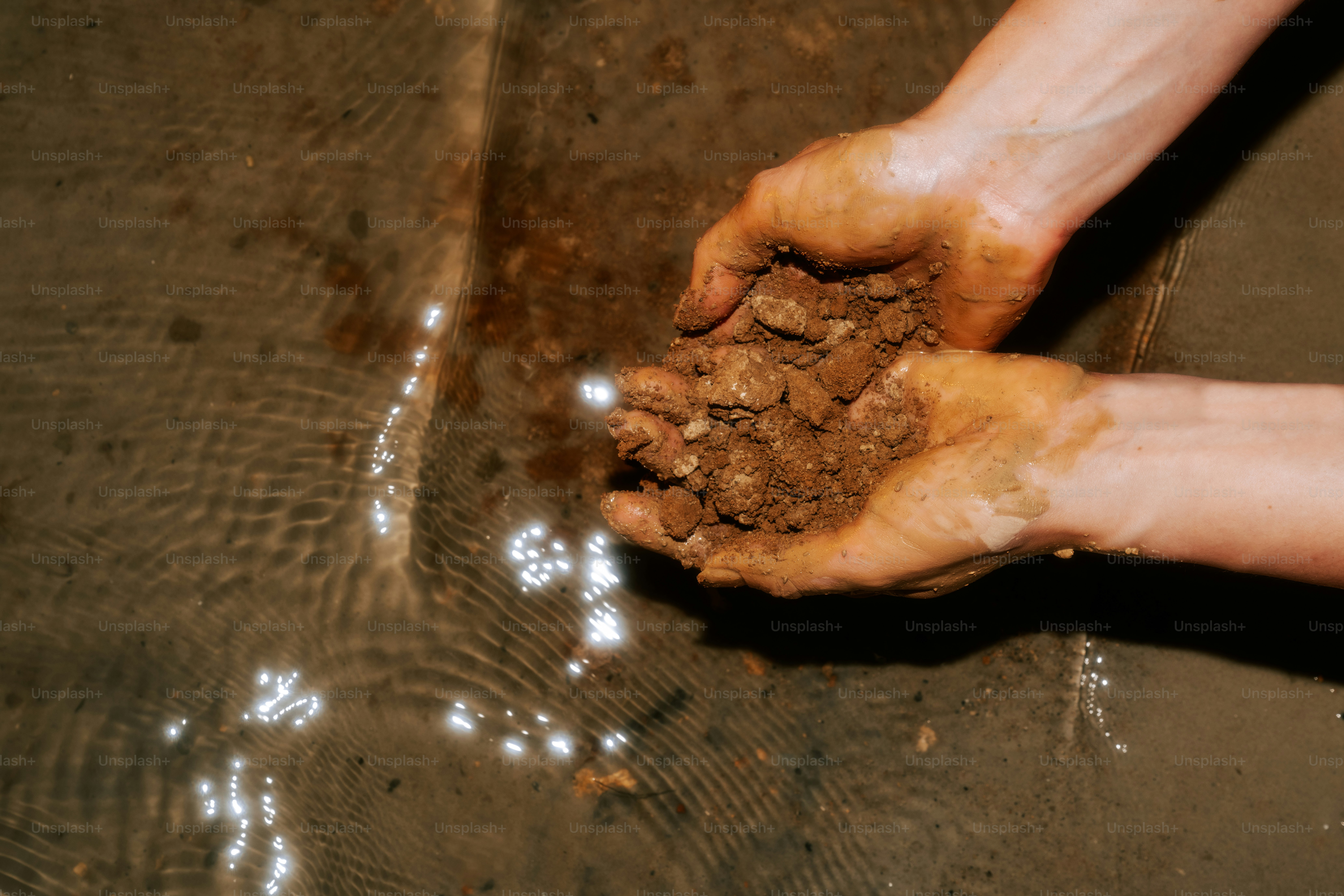 Hands holding soil near water.