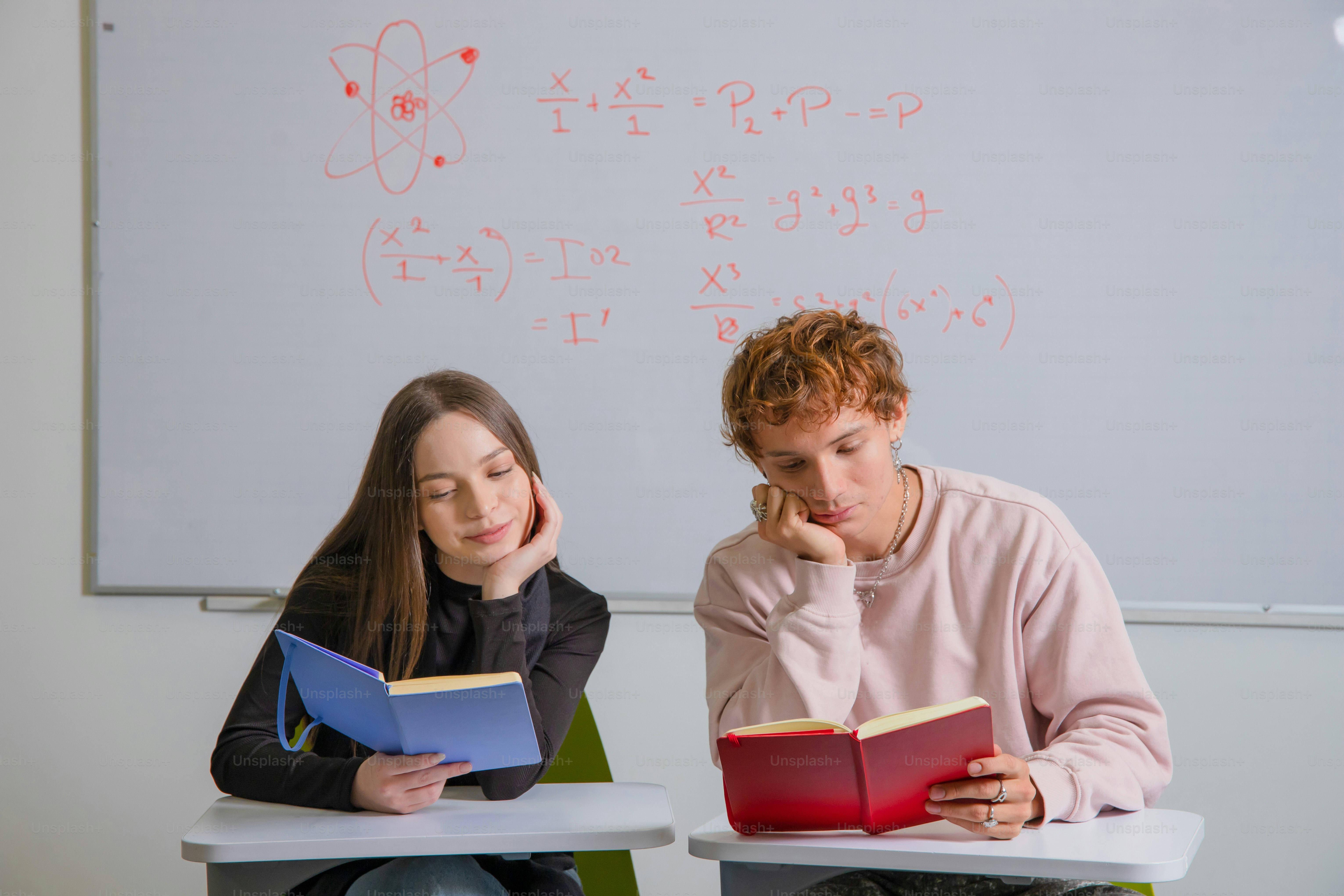 Two students study in a classroom with books.