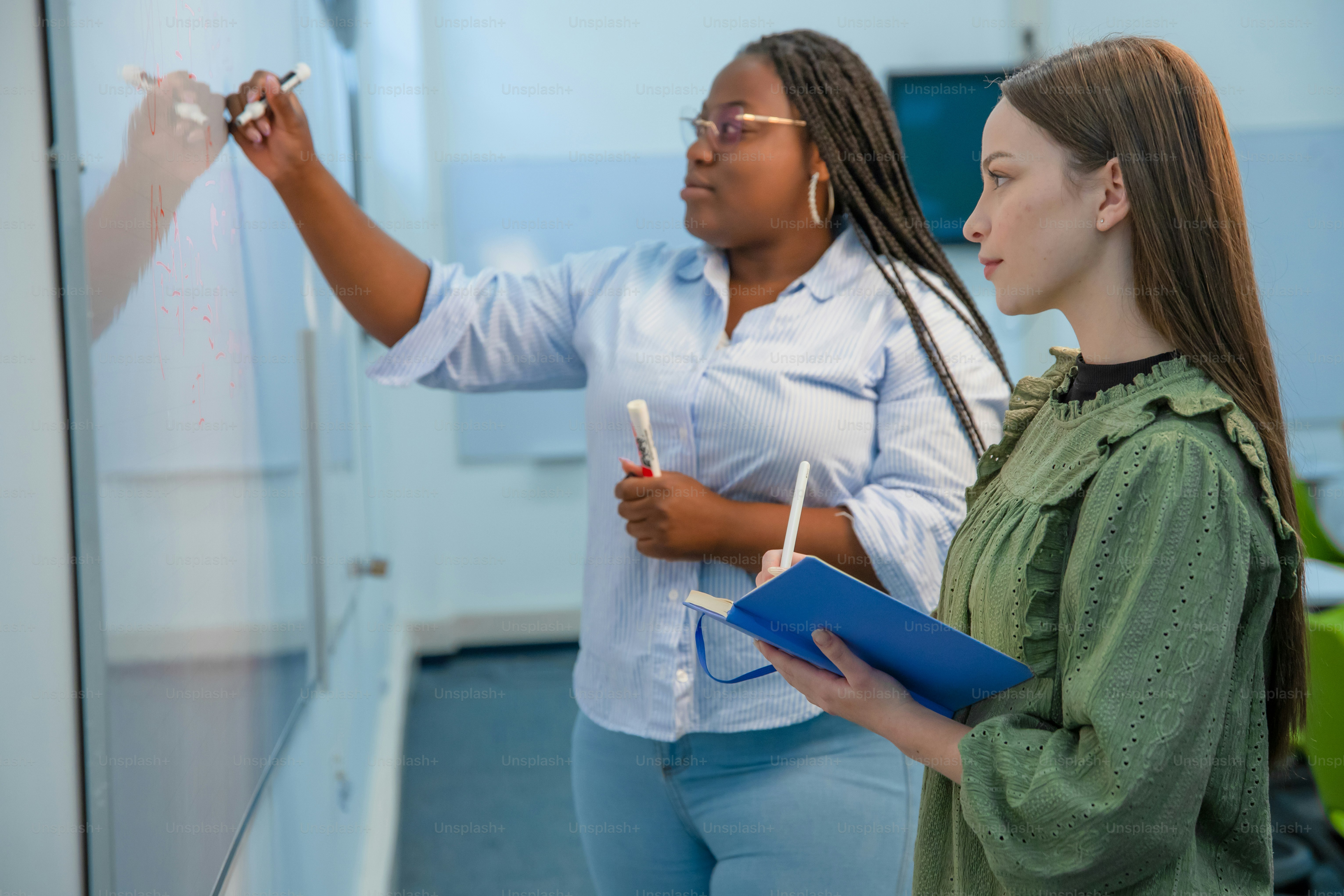 Two women collaborate by a whiteboard.