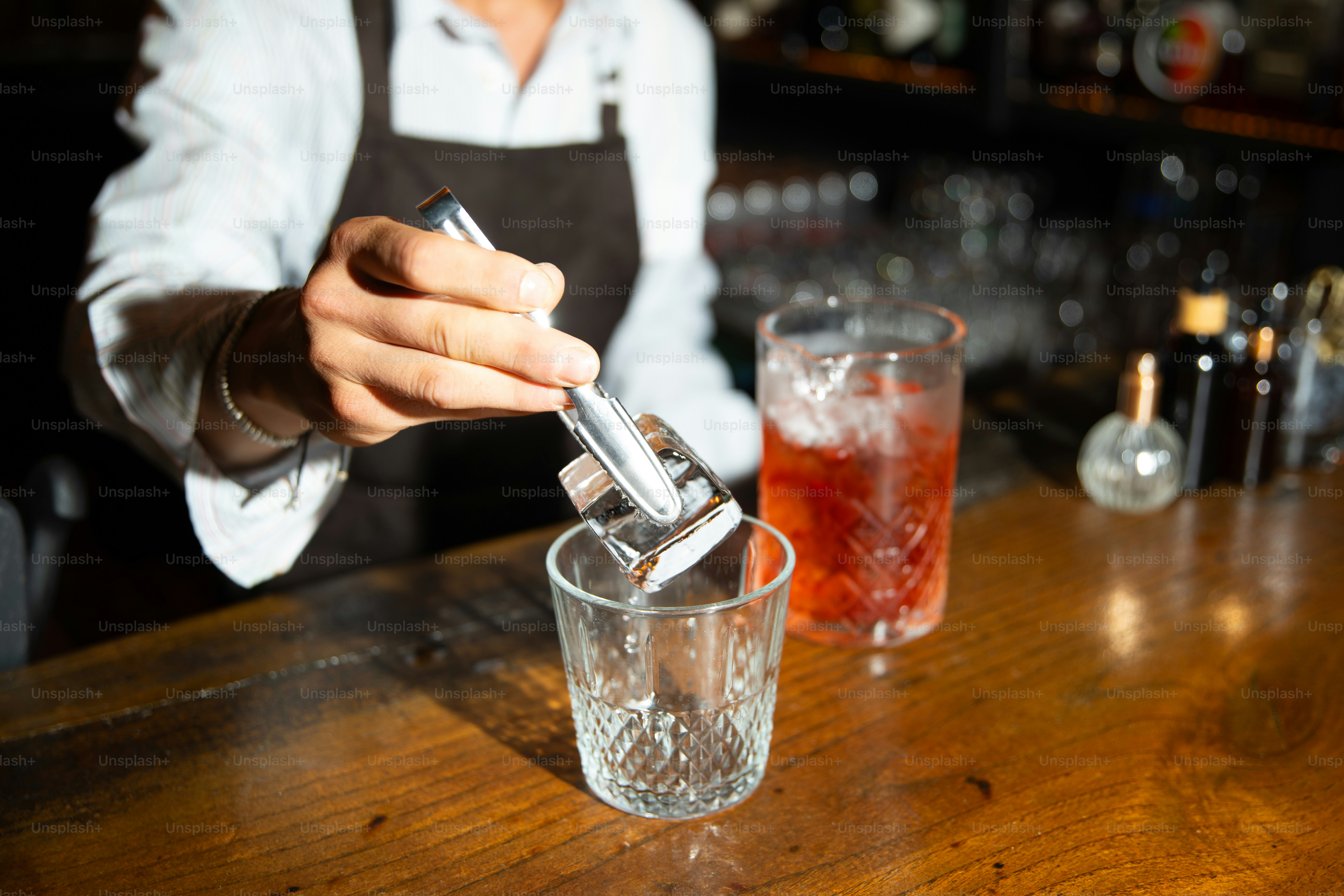 Bartender adds ice cubes to a glass.
