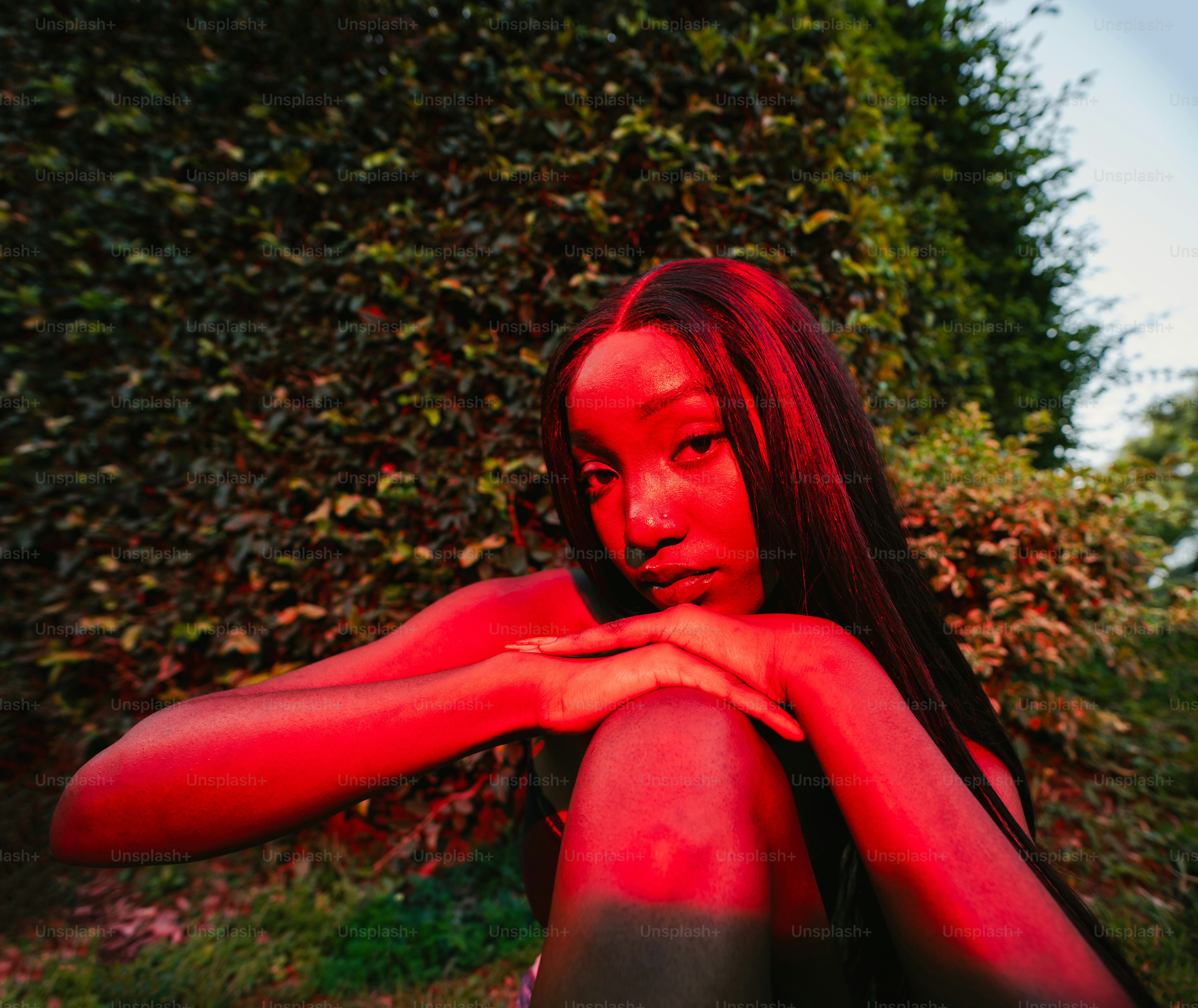 Uma mulher posa em um jardim iluminado em vermelho.