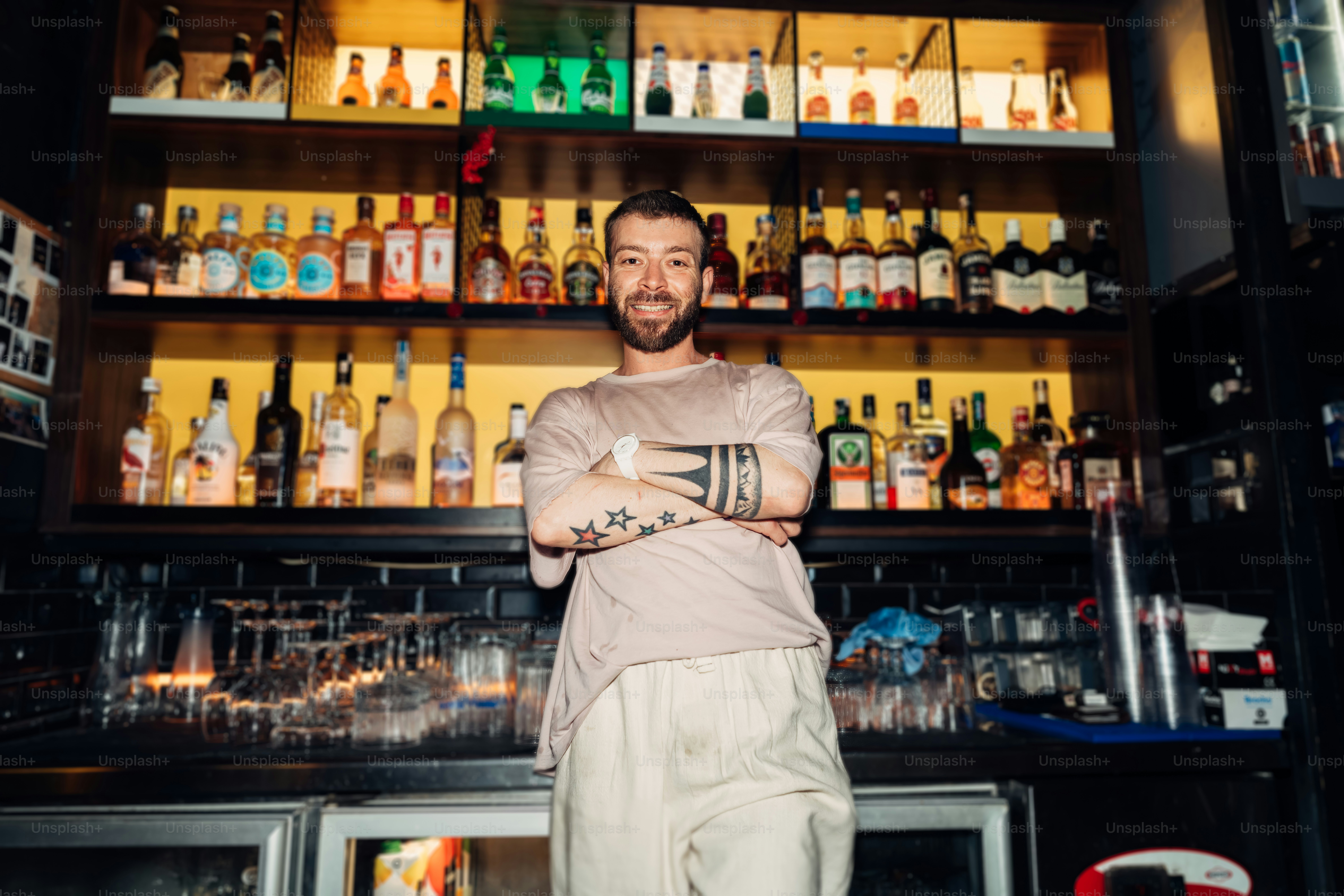 A bartender smiles in front of a stocked bar.