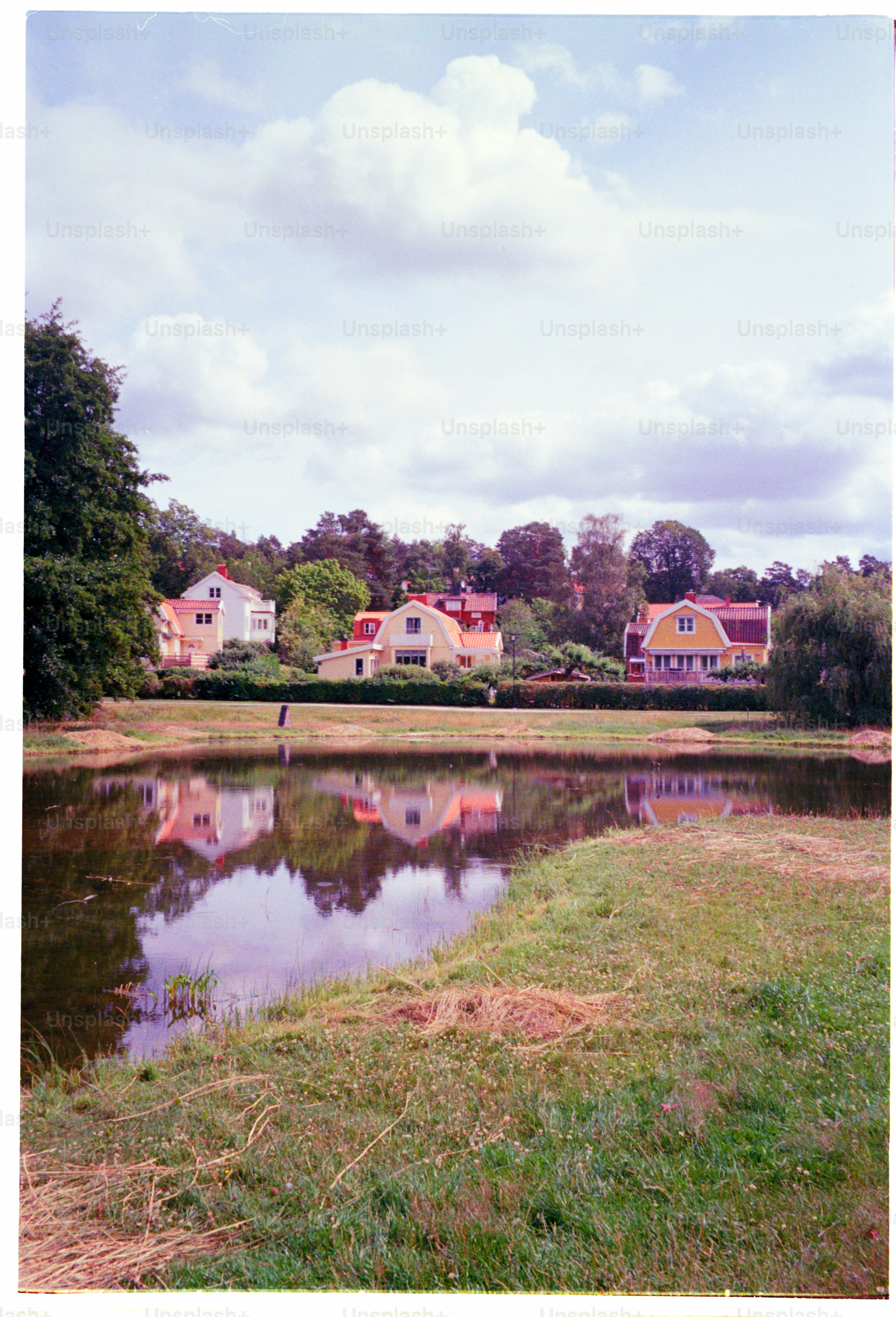 Houses reflect in calm water under cloudy skies.