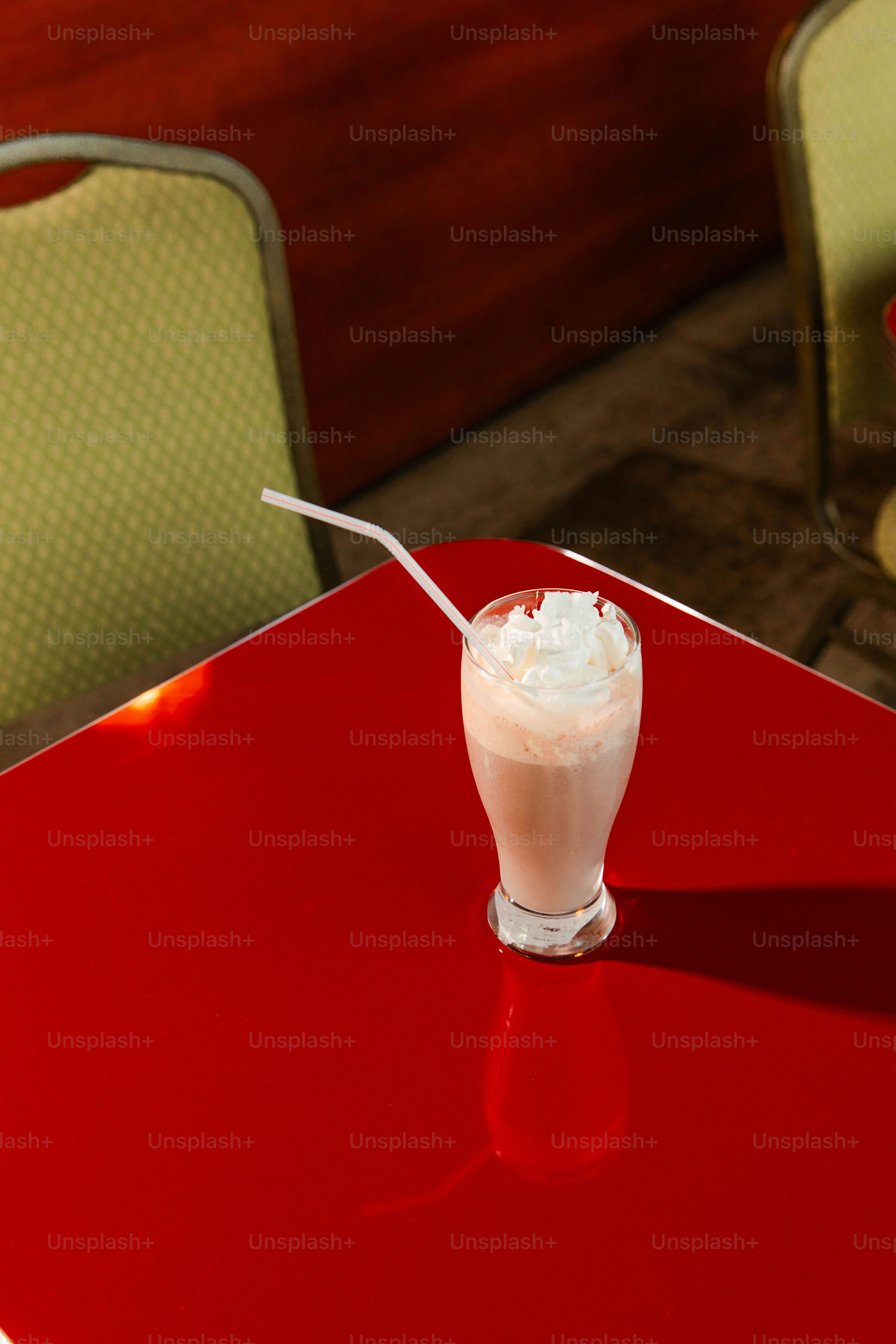 Milkshake with whipped cream sits on a red table.
