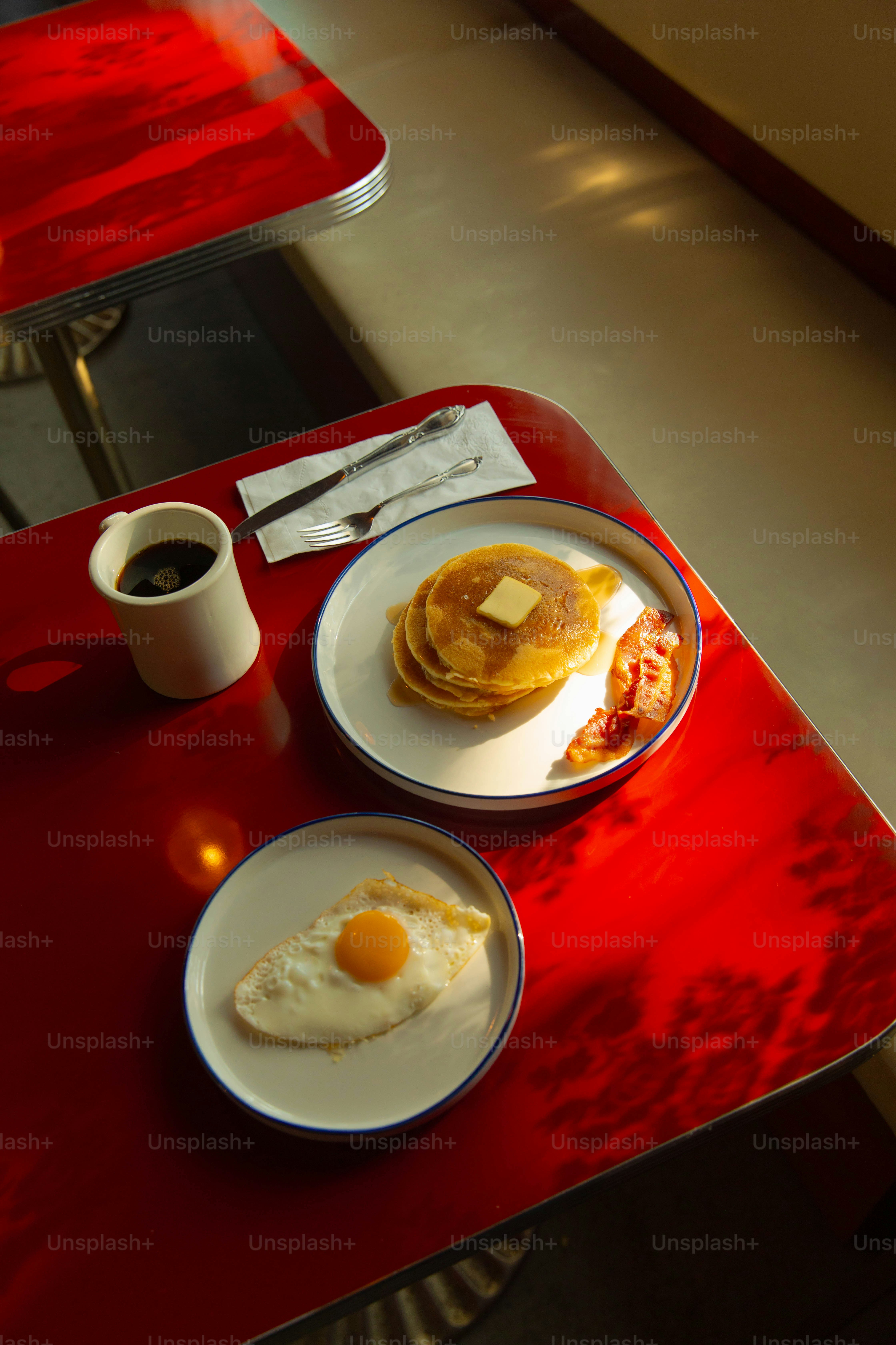 Breakfast of pancakes, eggs, and bacon on a red table.