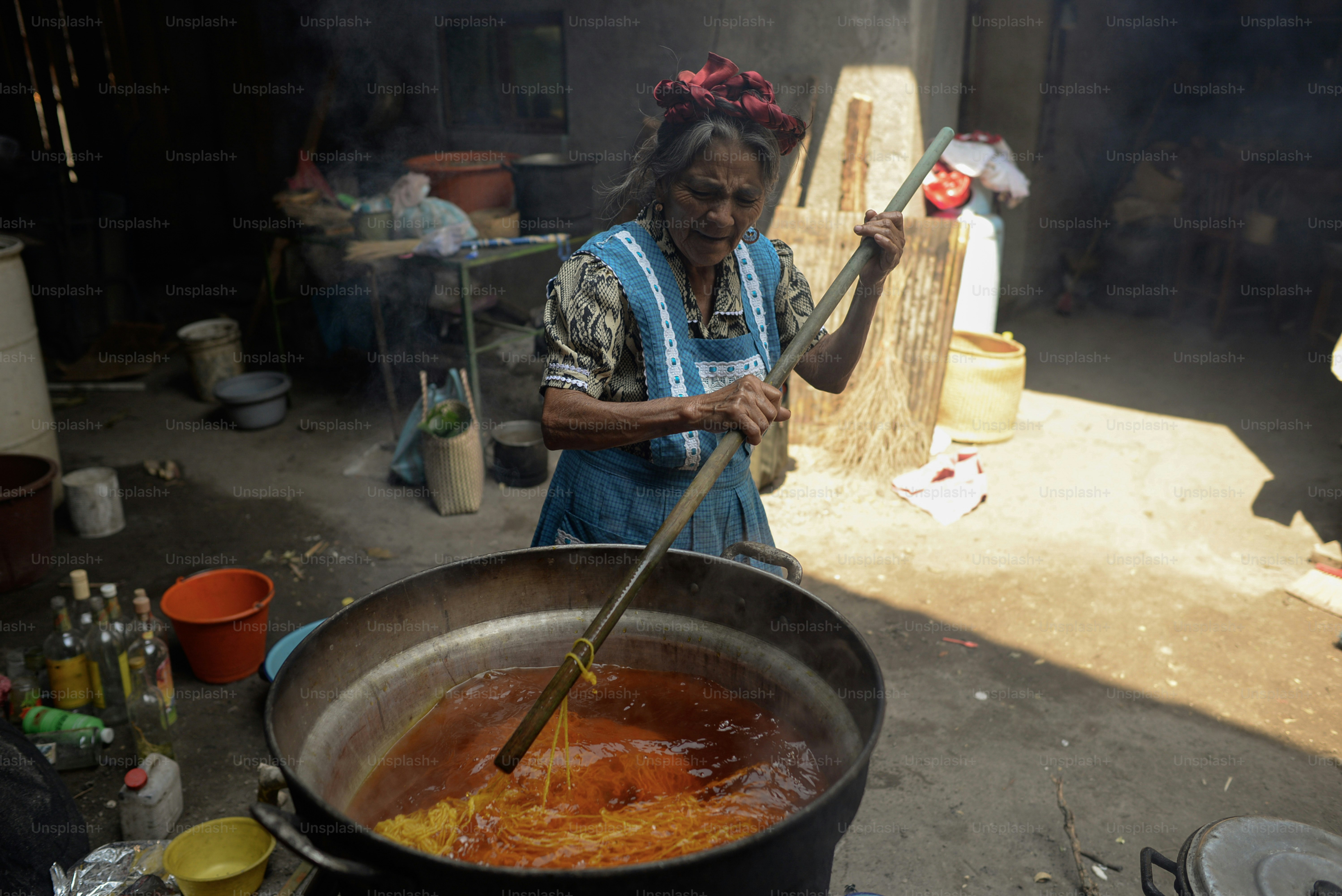 An elderly woman stirs a large pot.