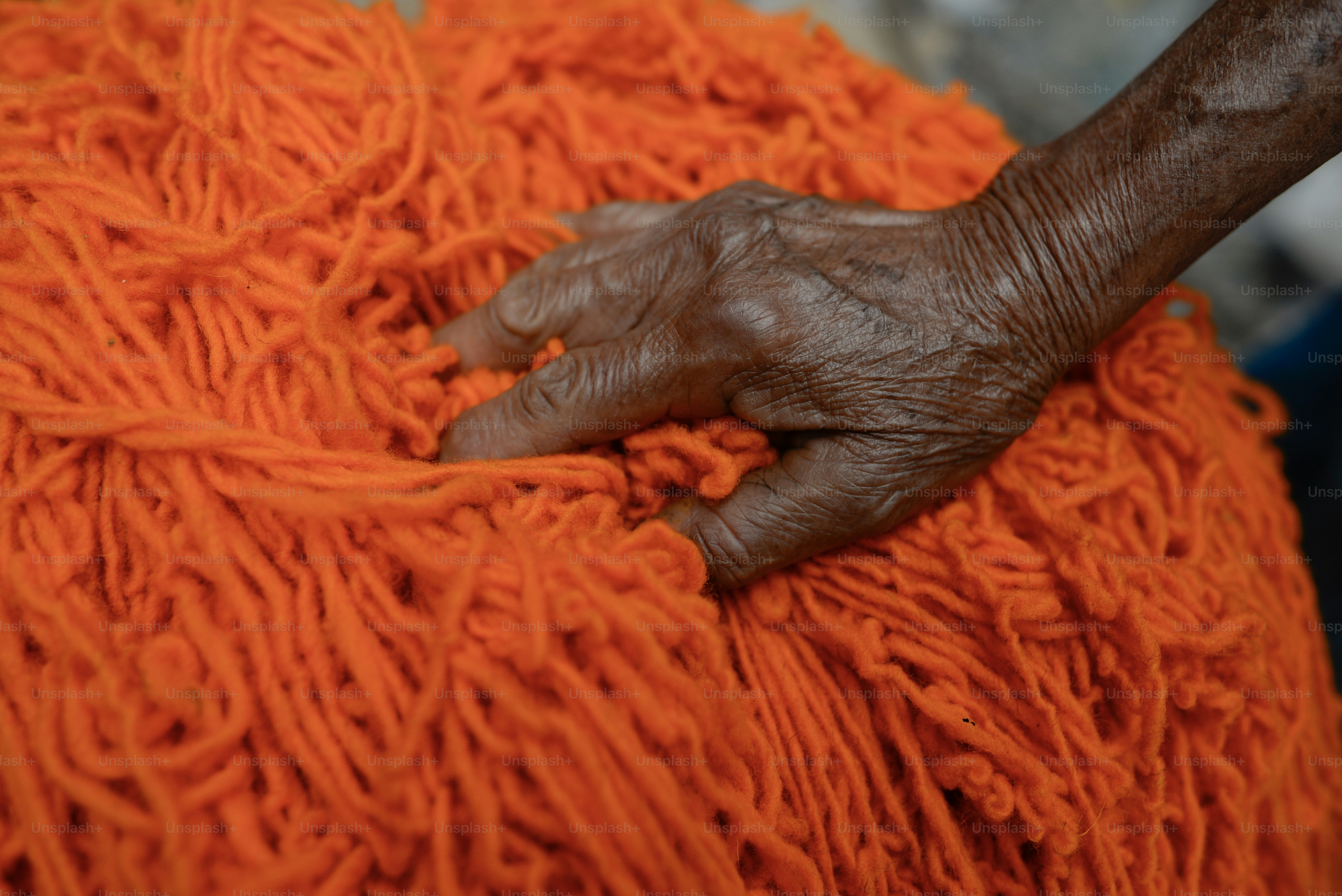 A hand touches a heap of bright orange yarn. photo – Indigenous Image ...