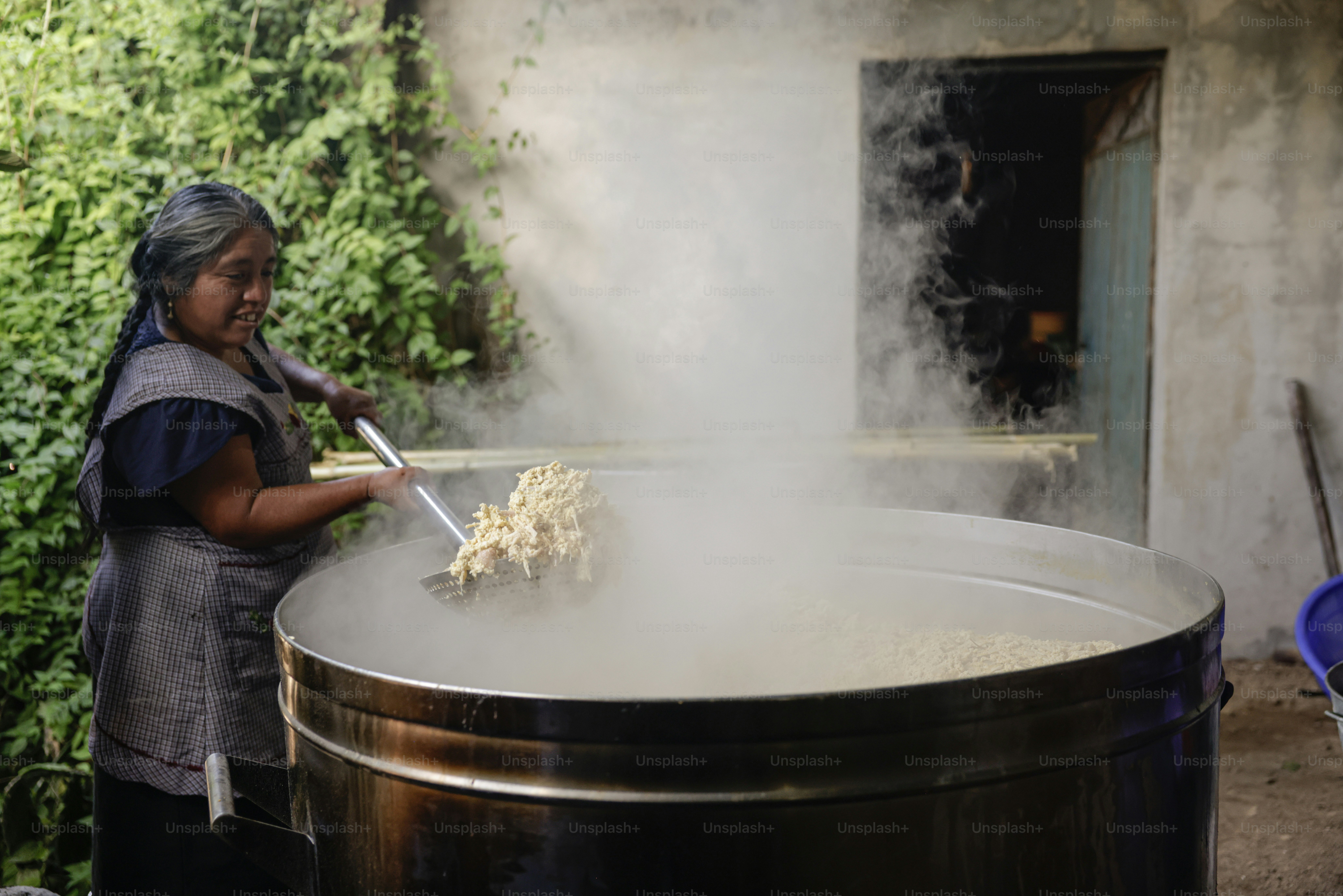 女性は湯気の立つ水の入った大きな鍋で食べ物をかき混ぜます。