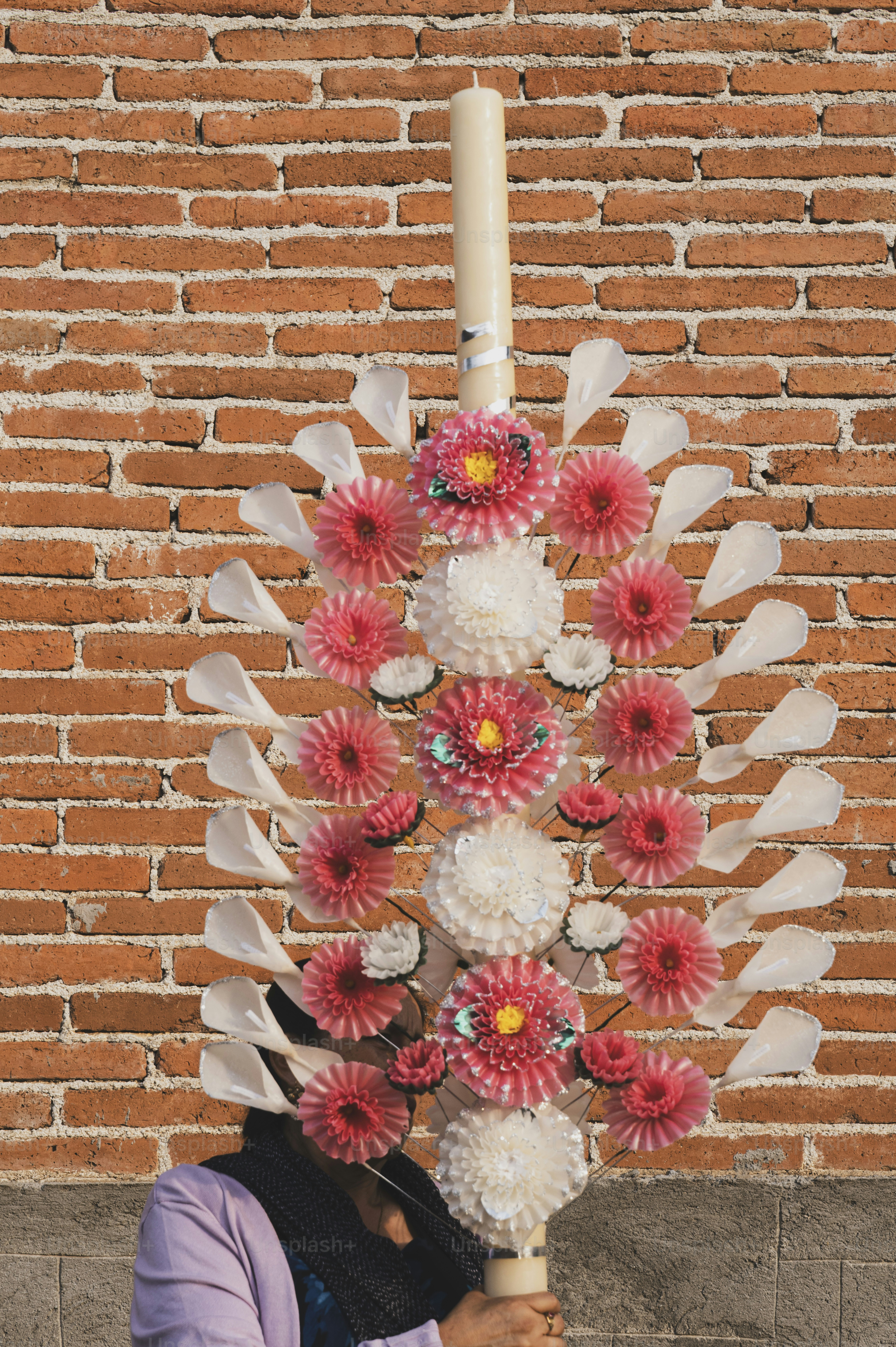 A decorated candle stands in front of a brick wall.