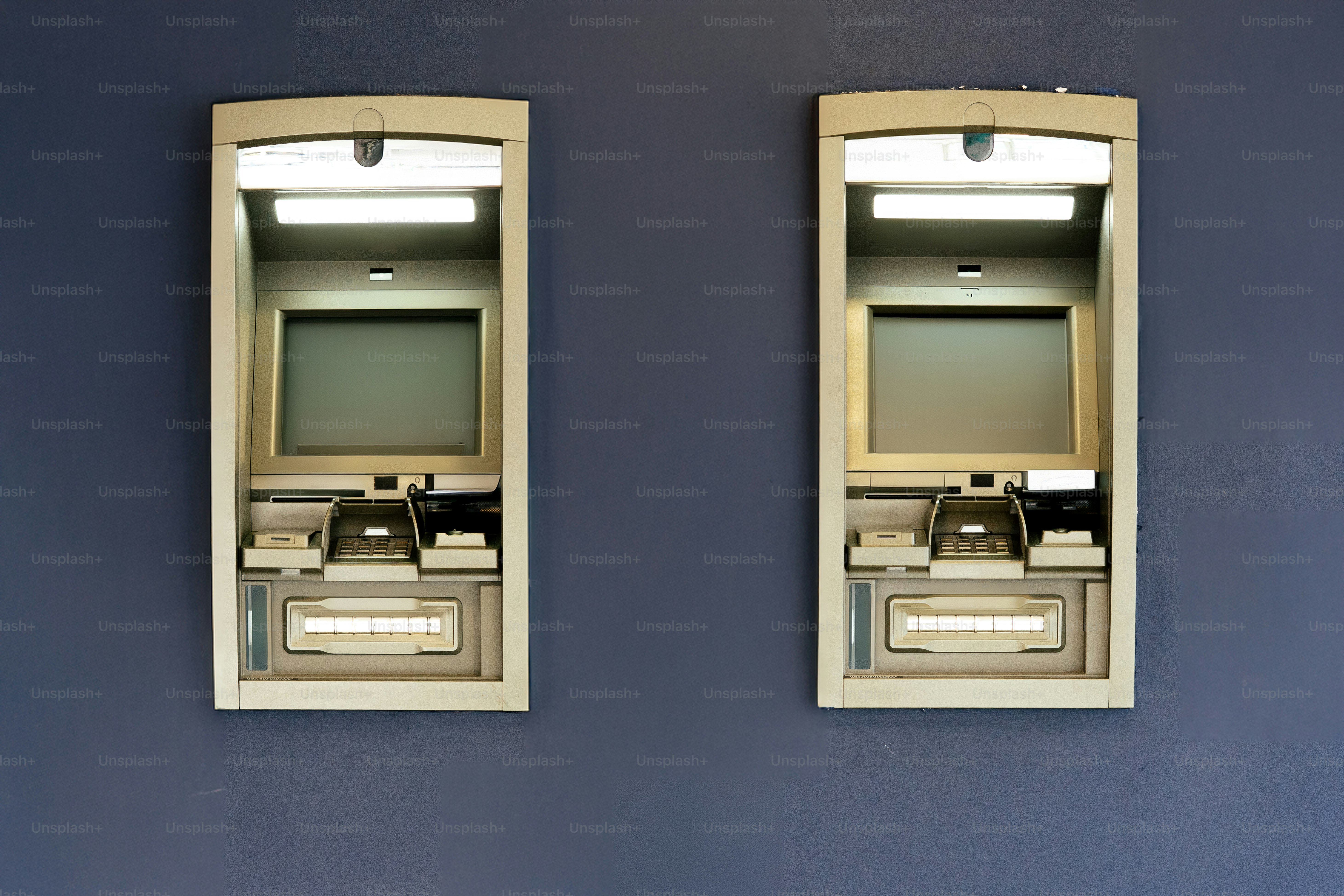 Deux distributeurs automatiques de billets identiques montés sur un mur bleu.