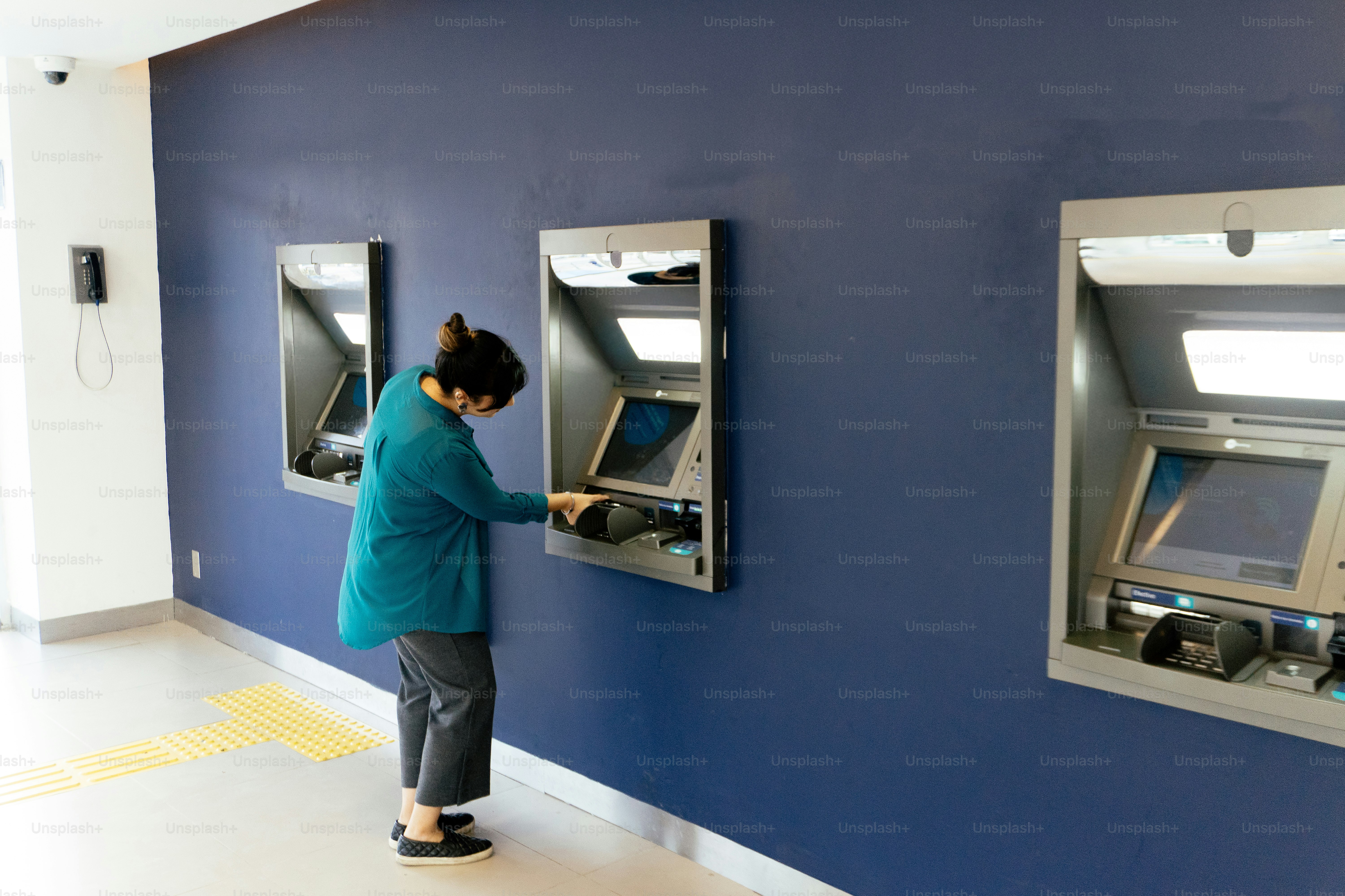 Woman uses atm machine on blue wall