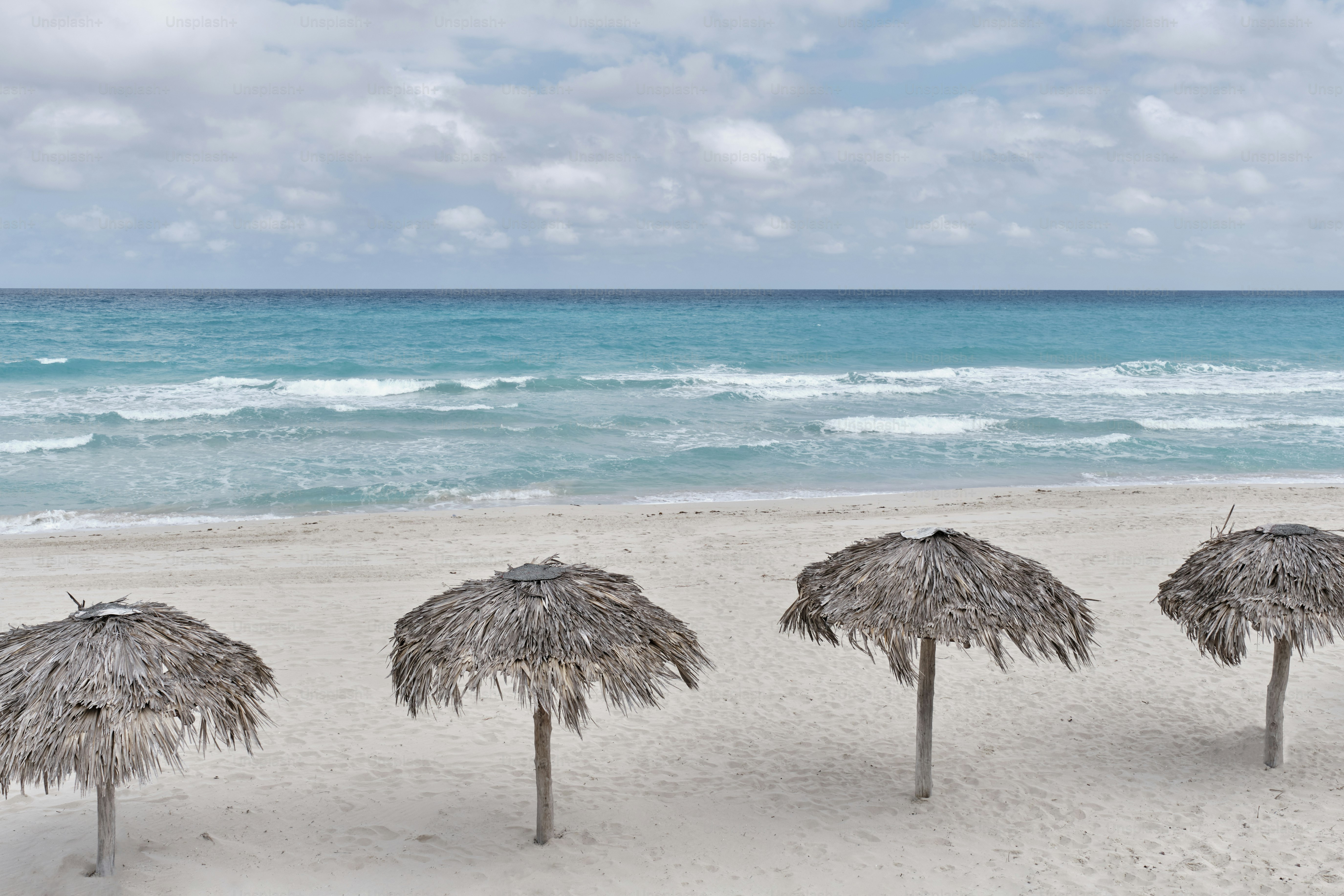 Atlantic sandy beach of Cuba, resort Varadero. Four palm leaf sun umbrellas. Waves and cloudy sky. Scenic seascape.