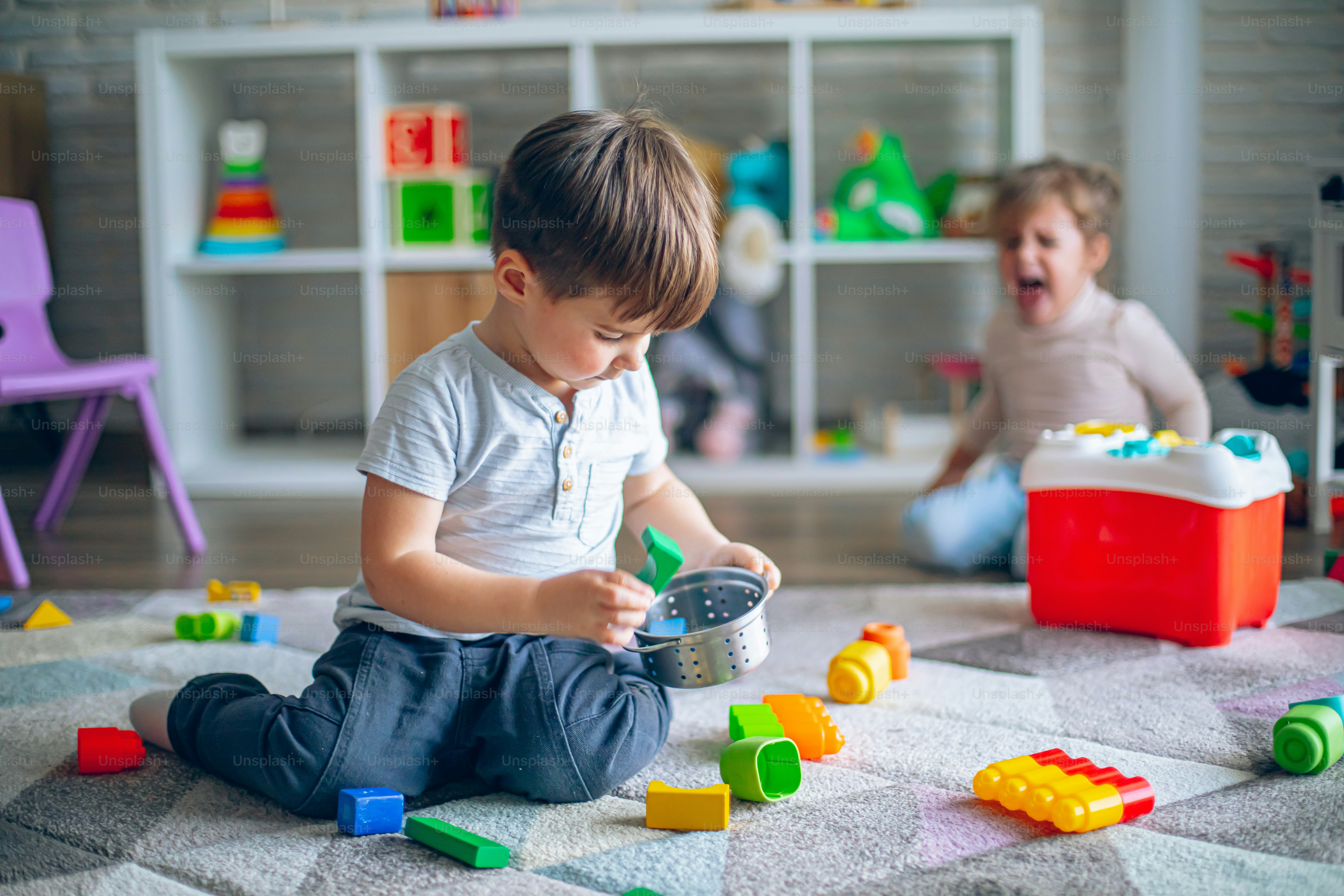 A little boy makes a mess with his toys while a little girl cries