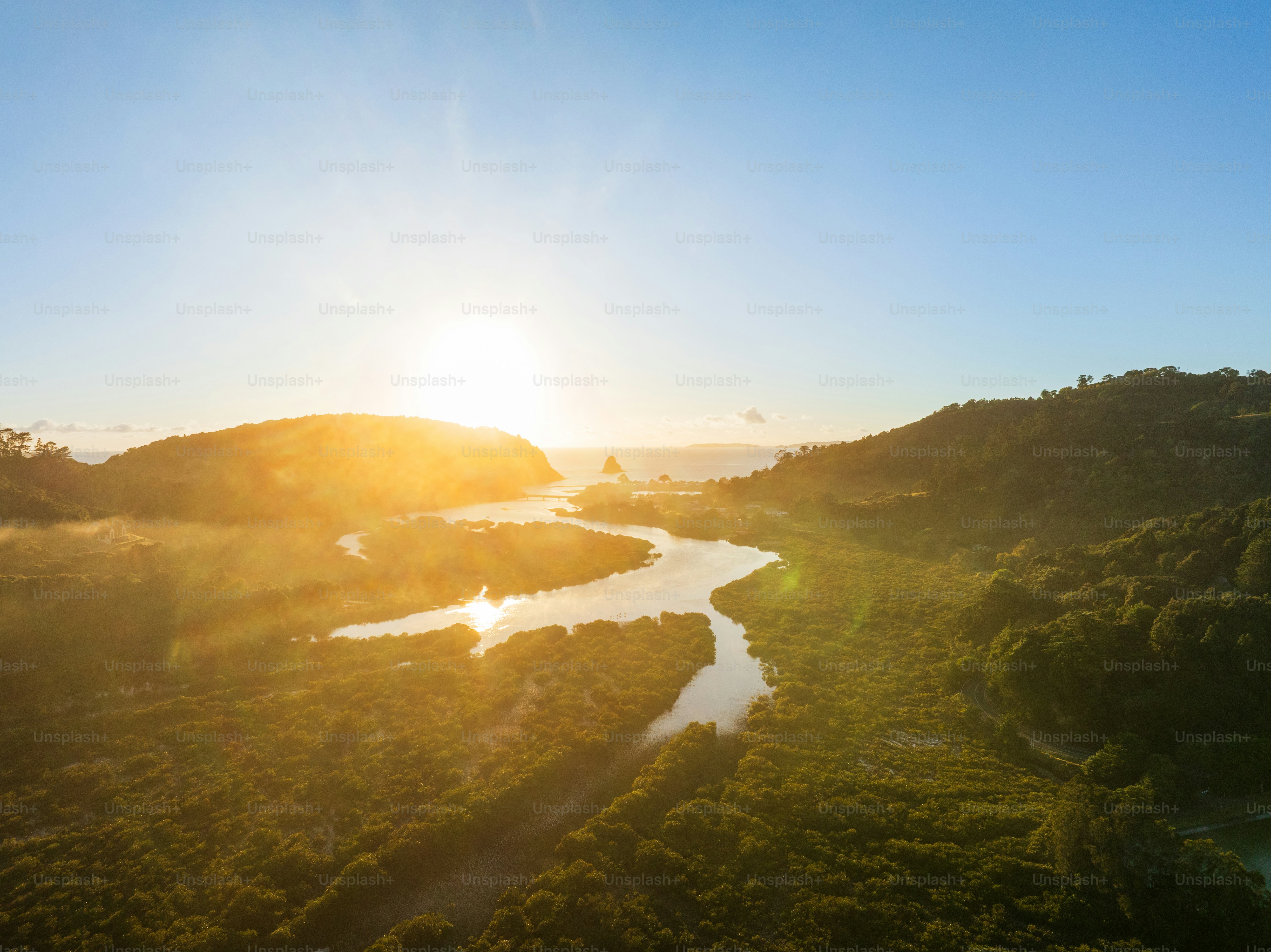 Malerischer Blick auf ein wunderschönes natürliches Gewässer mit üppigen grünen Hügeln bei Sonnenaufgang mit blauem Himmel im Hintergrund.