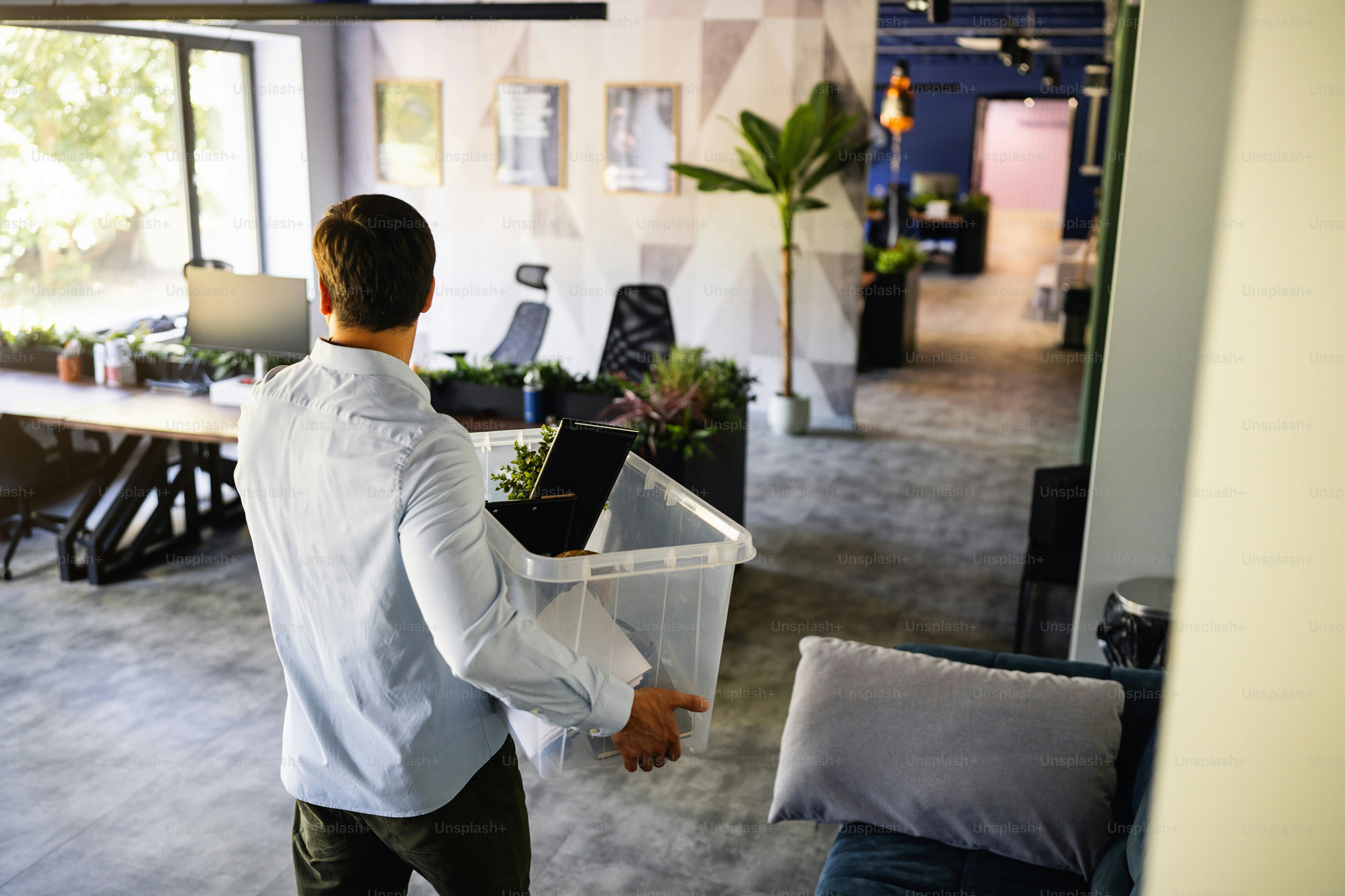 Rear-view of an unrecognizable young Caucasian businessman carrying his office belongings into a plastic box, while leaving work because he gets fired or quit a job