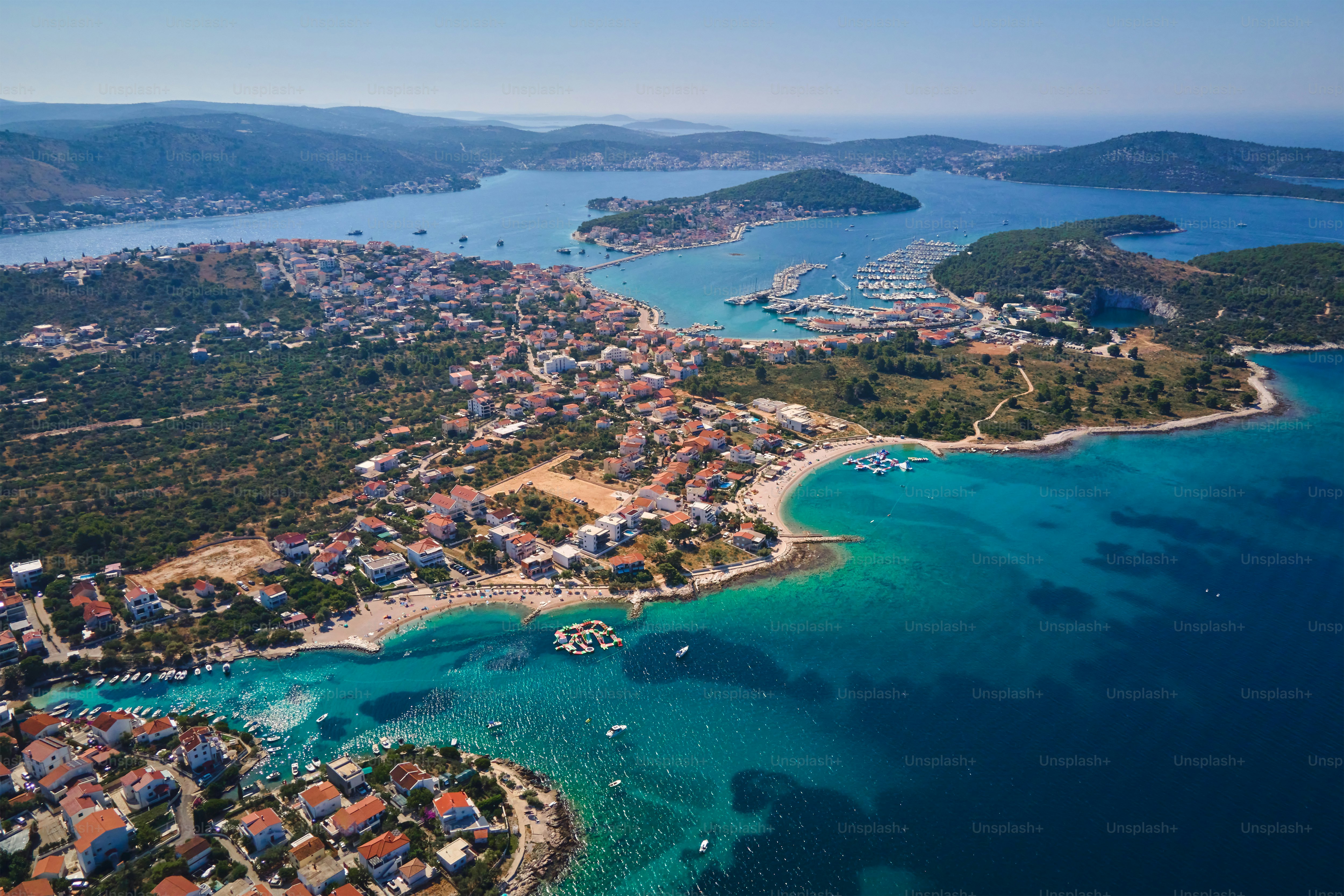 Pulau-pulau di laut ditutupi dengan tanaman hijau subur dan rumah, pemandangan udara. Tempat wisata untuk liburan musim panas. Lanskap panorama garis pantai laut Adriatik dekat kota Rogoznica di wilayah Dalmatia, Kroasia