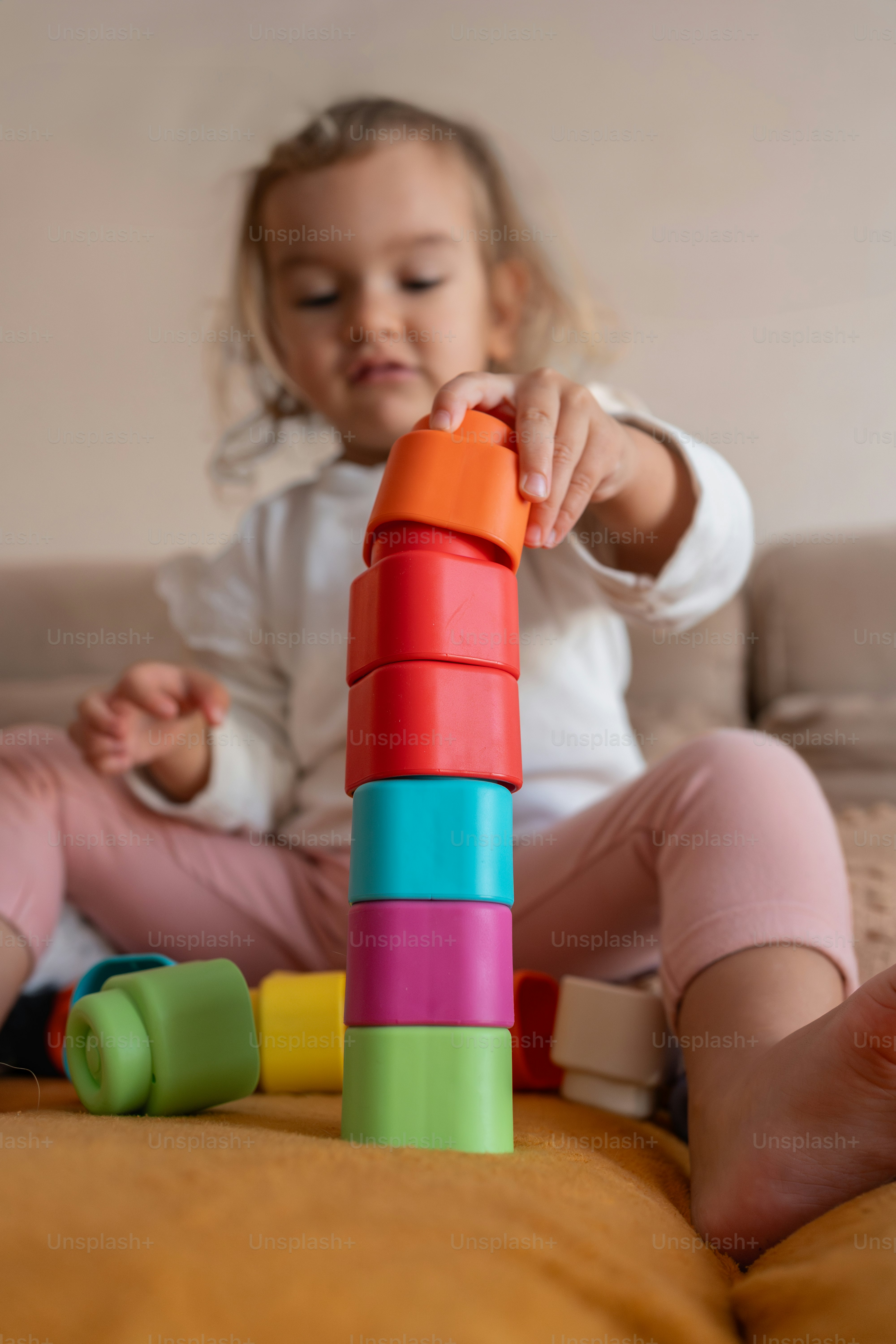 La ragazza impila con cura i giocattoli colorati su un divano, creando una torre alta e vibrante
