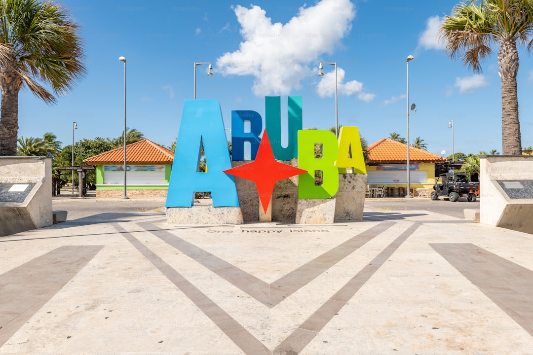 Colorful Aruba sign with tropical palm trees and blue sky. Popular travel destination for tourists. Bright monument in a