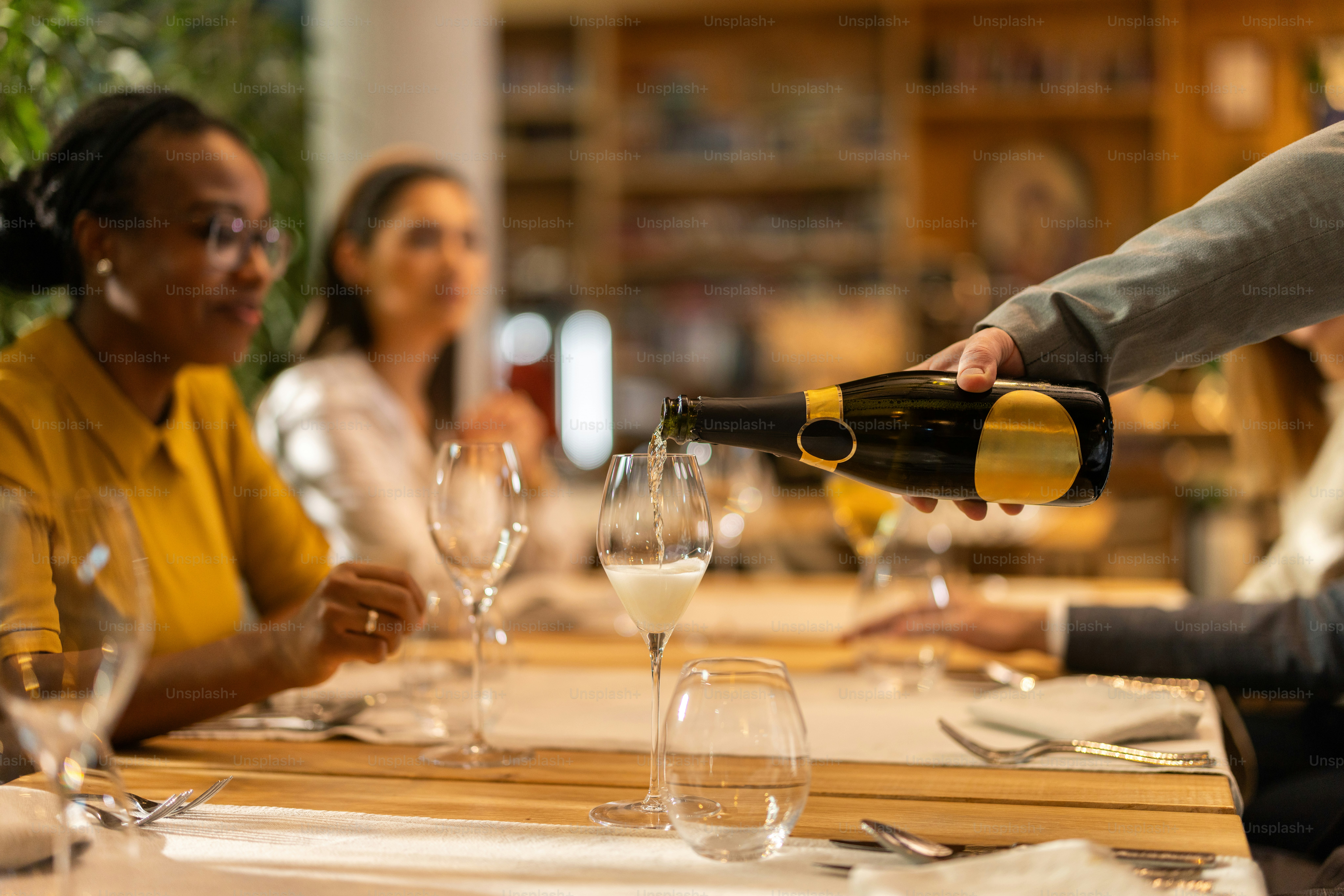 Close-up shot of unrecognizable waiter pouring white wine into wine glass for a multiracial group of guests in a luxurious hotel restaurant
